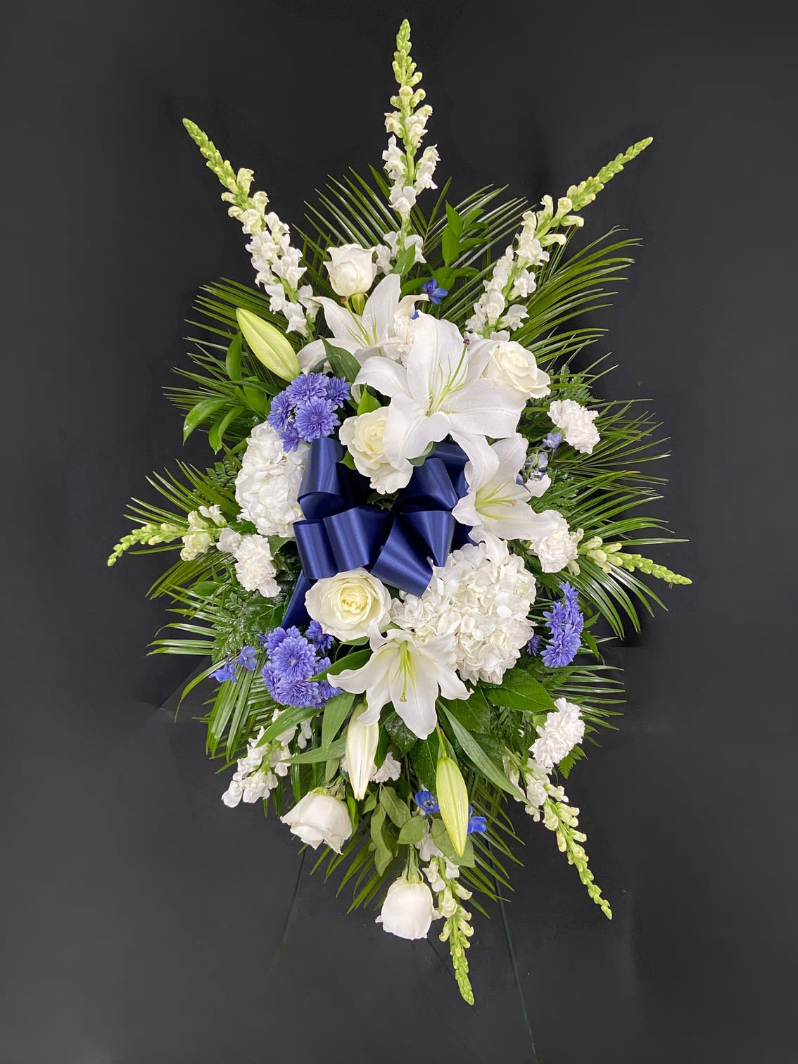 Dark Blue &amp; White Standing Spray - Dark Blue Delphinium and Daisy Poms are accompanied by White Oriental Lilies, White Roses, White Hydrangeas, White Carnations and White Snapdragons. Arrangement is mounted on a 4.5ft standing easel for prominent display at funeral services.