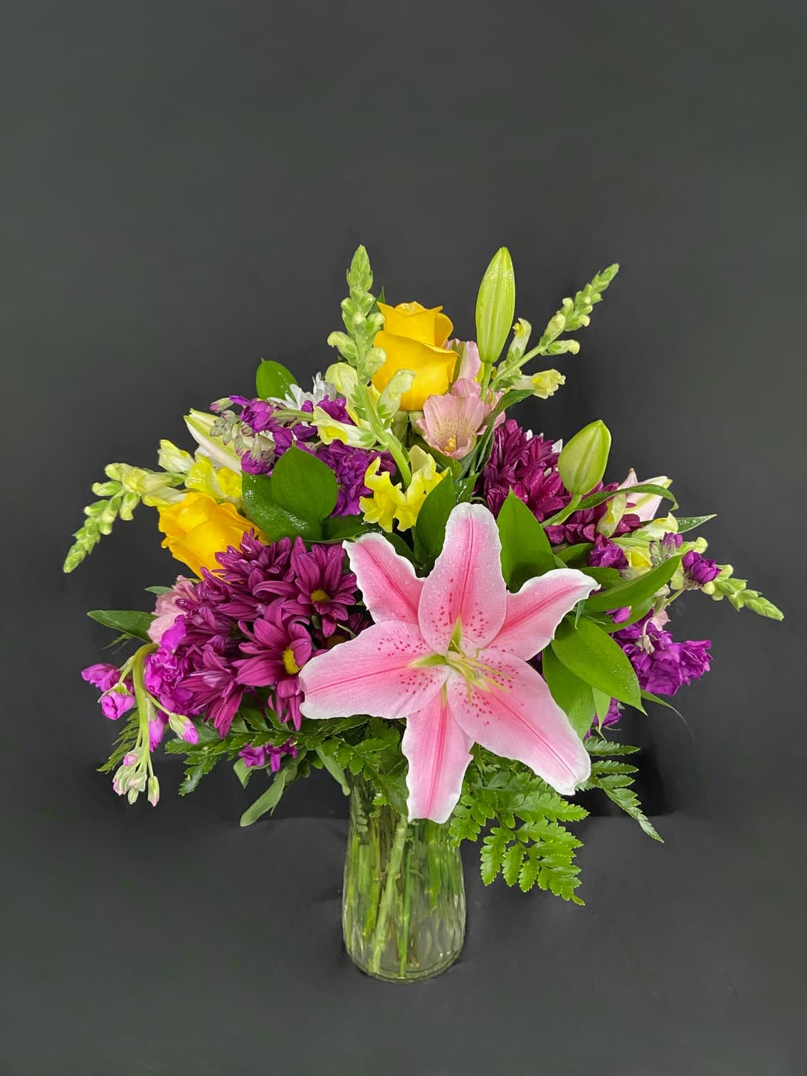 Pink lily and mixed purple-yellow flowers in a clear glass vase