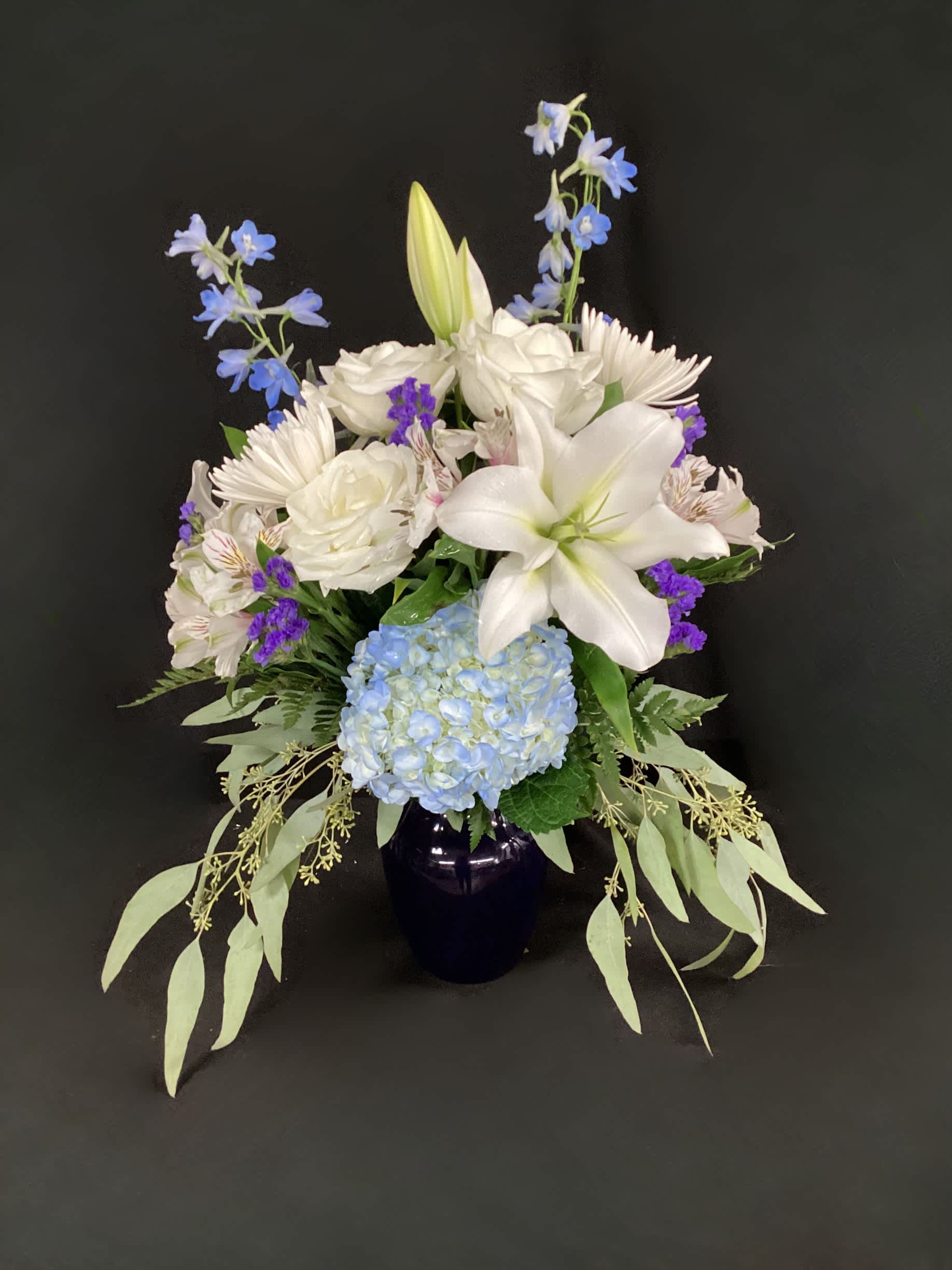 White lilies and blue hydrangea in a dark vase