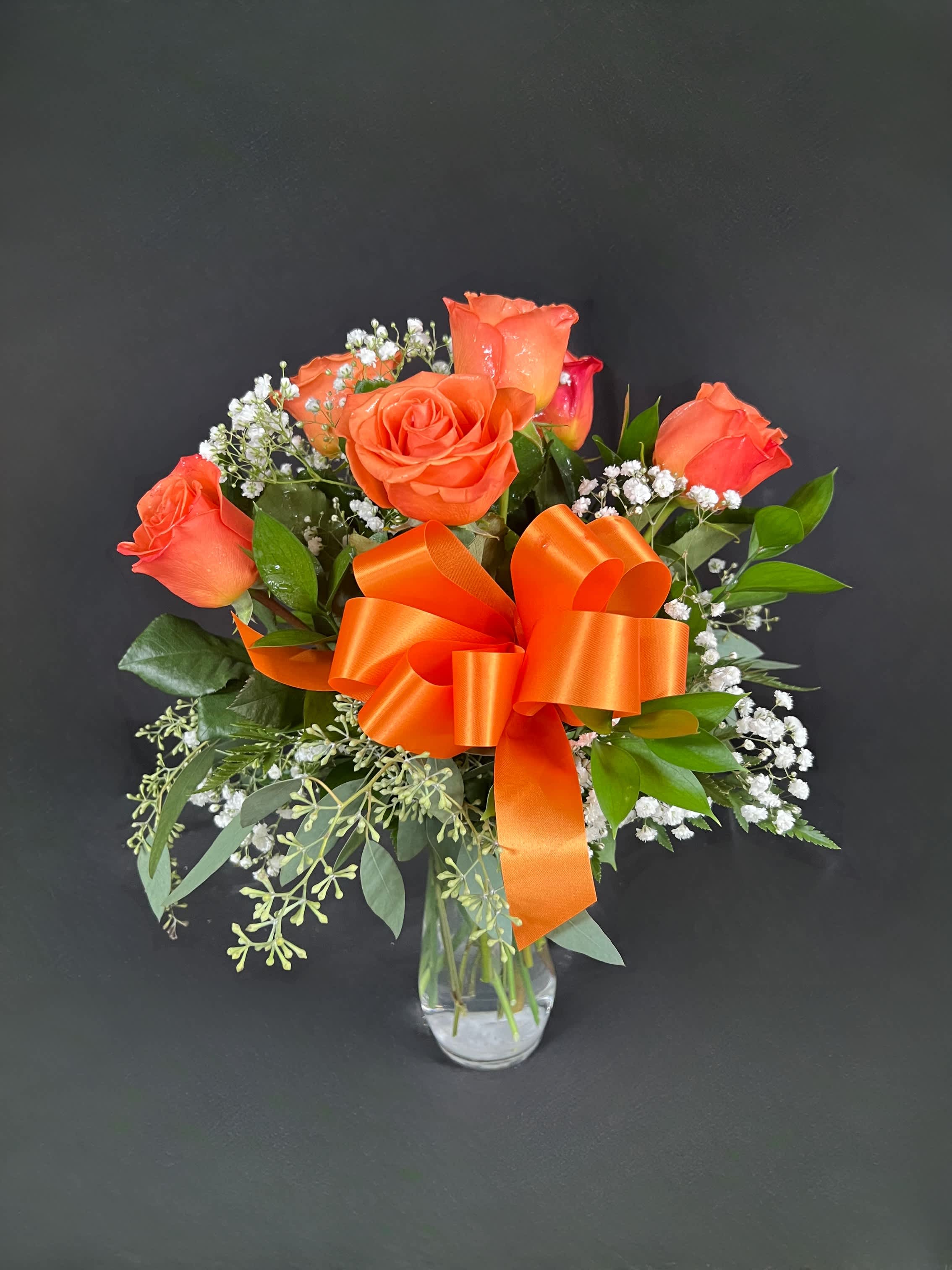 Orange rose bouquet in a clear glass vase with an orange ribbon