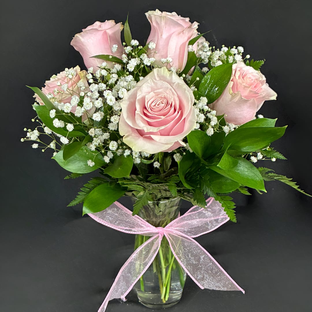 Pink roses with baby's breath in a clear glass vase tied with a pink ribbon