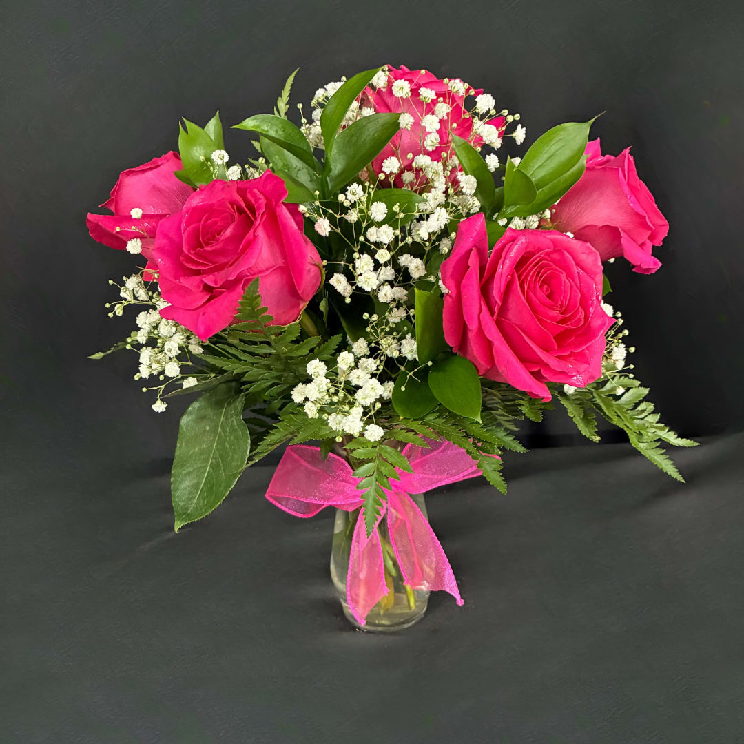 Pink roses with baby's breath in a clear glass vase tied with a pink ribbon