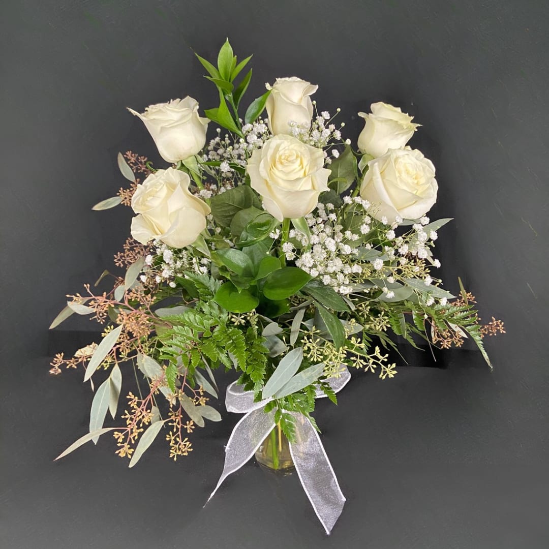 White roses arranged in a glass vase with baby's breath and greenery
