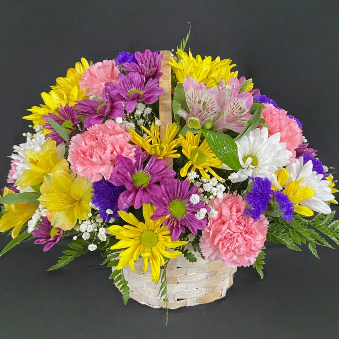Mixed bouquet of yellow, purple, pink, and white flowers in a woven basket
