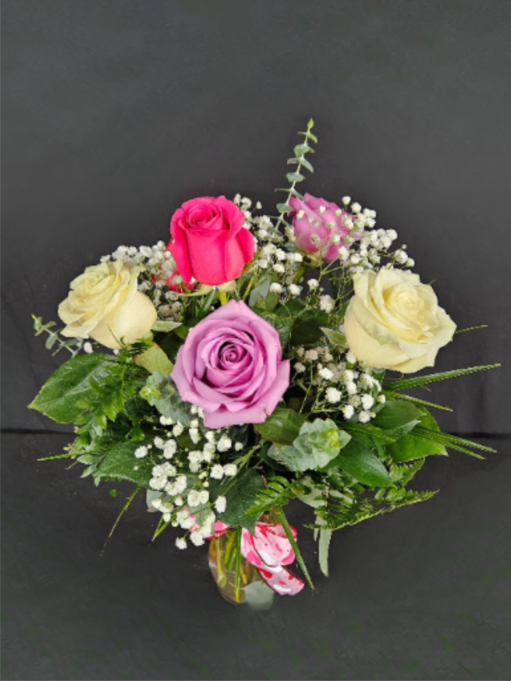 Small vase arrangement of cream, pink, and lavender roses with white filler flowers.