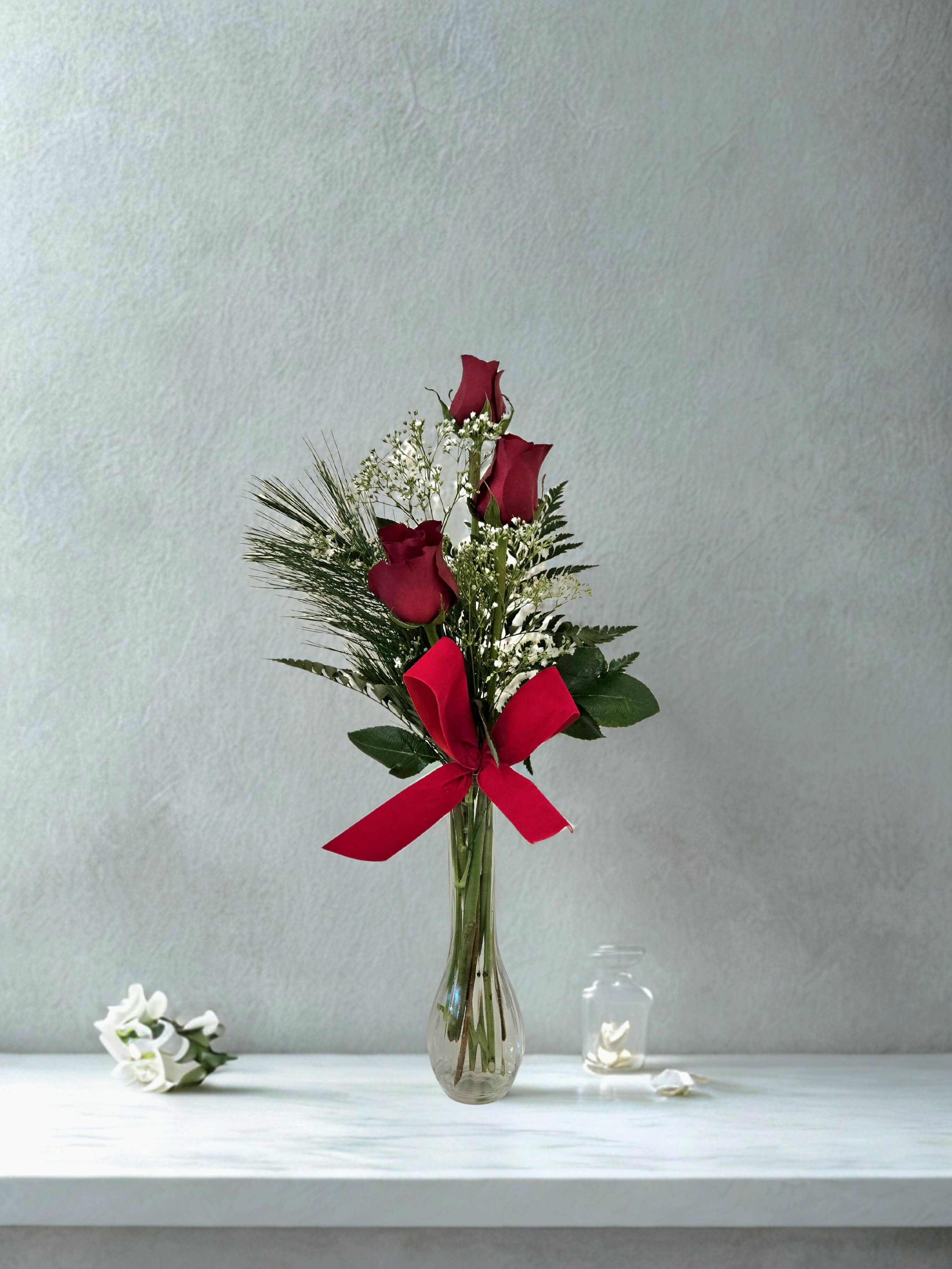 Red roses in a clear glass vase with a red ribbon