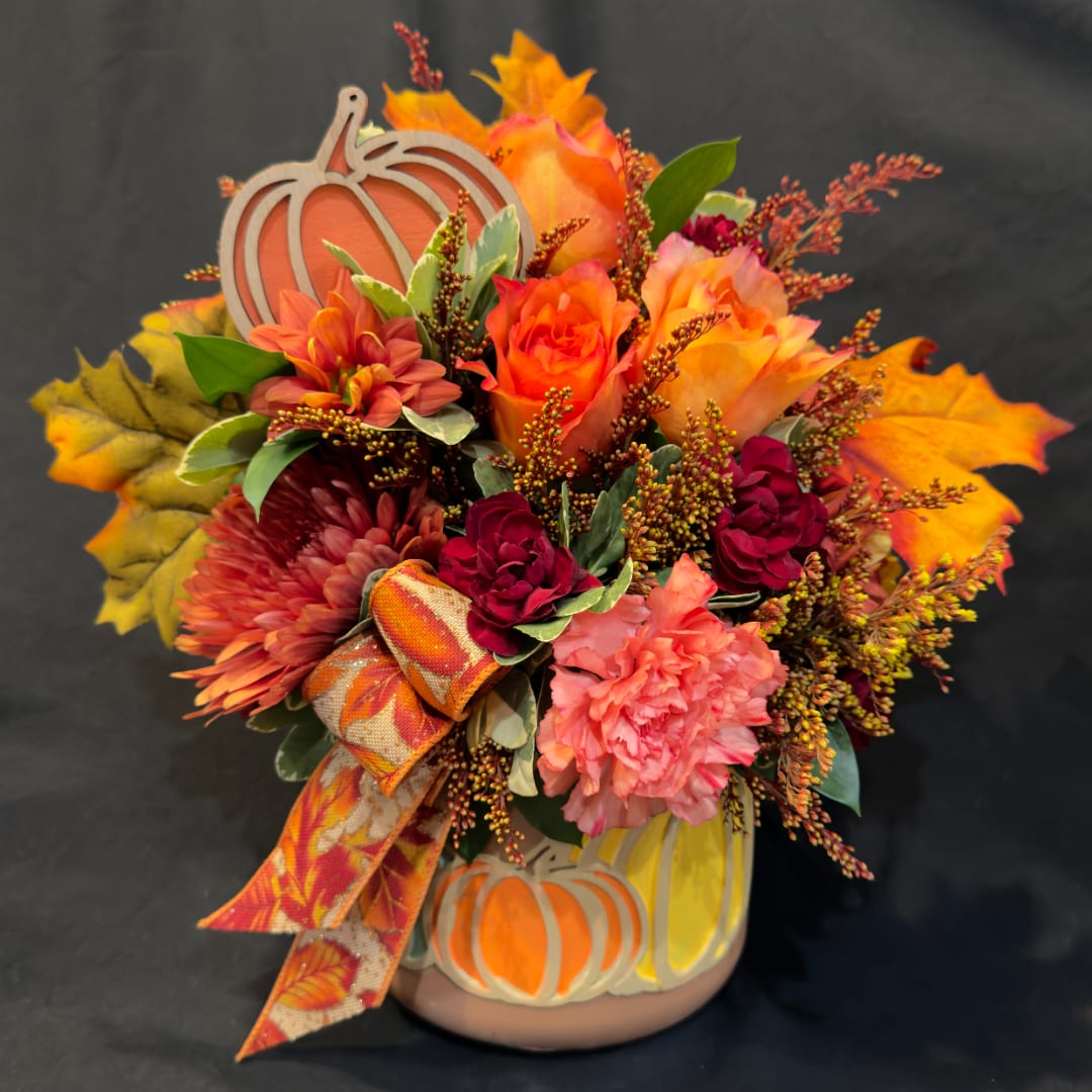 Autumn floral arrangement in a pumpkin vase with orange, pink, and burgundy blooms