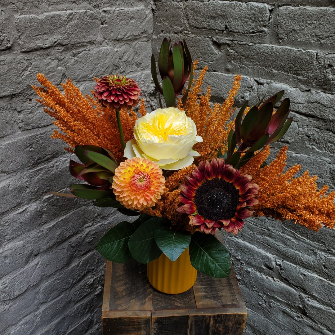 Mixed floral arrangement in a yellow vase with orange accents