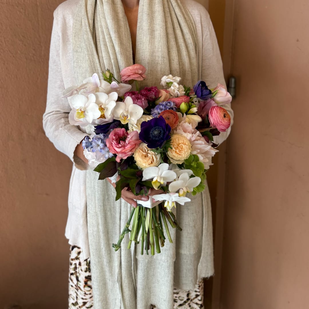 Woman holding a colorful wedding bouquet with orchids, roses, and ranunculus