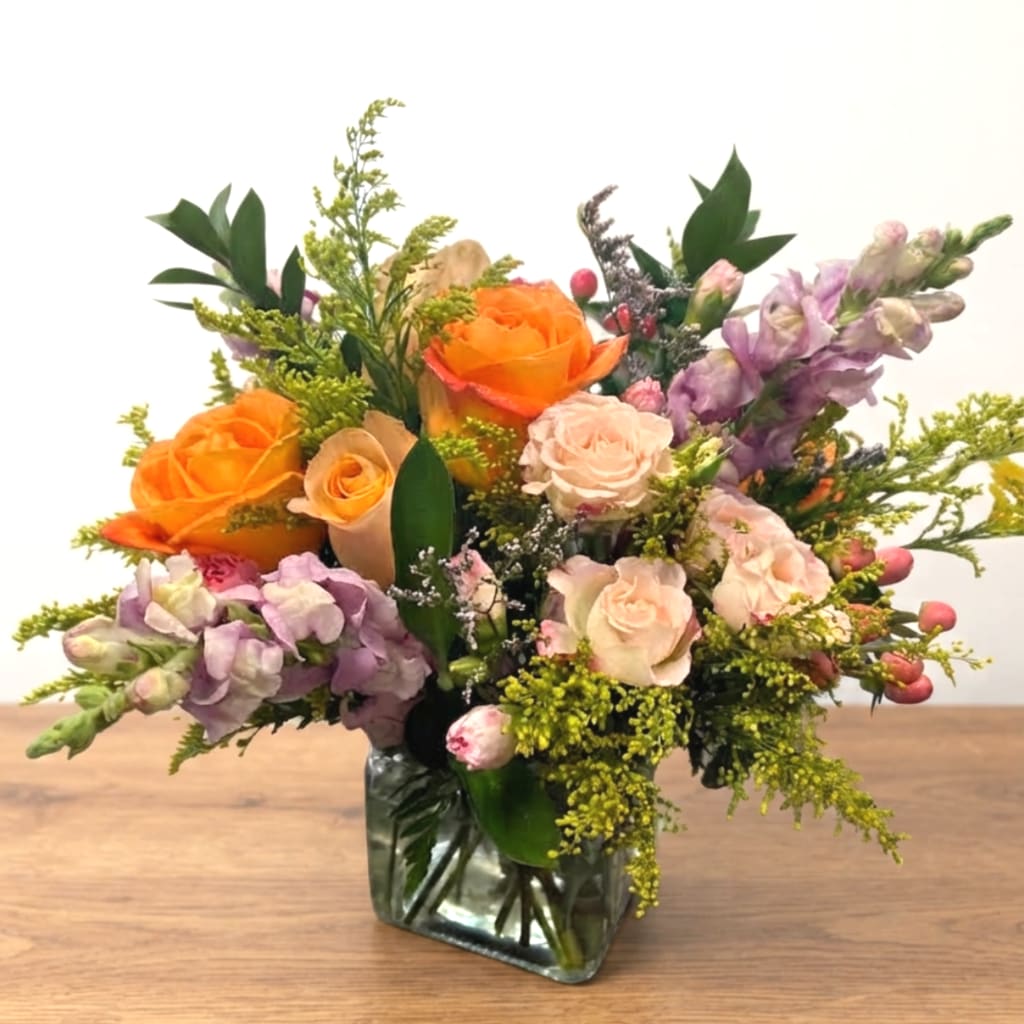 Mixed bouquet of orange and blush roses in a square glass vase