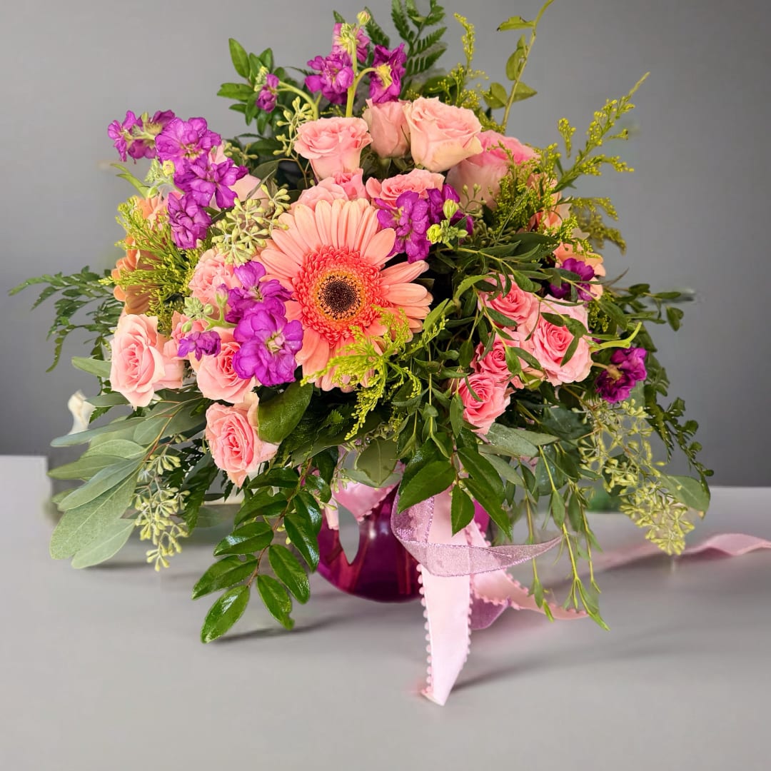 Pink roses and purple flowers arranged in a vase with a peach gerbera daisy
