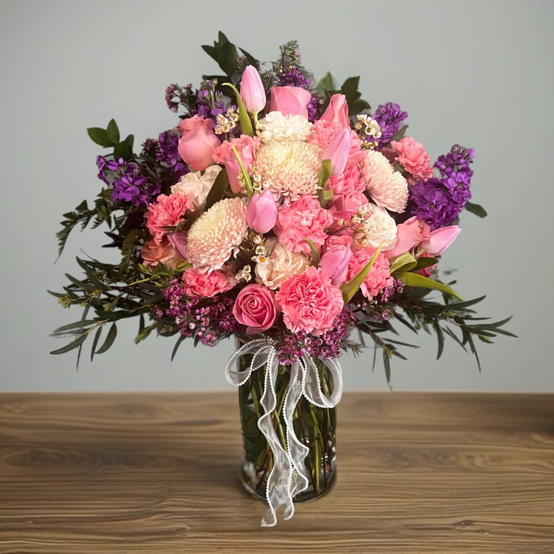 Pink and purple mixed flower bouquet in a glass vase with a white ribbon