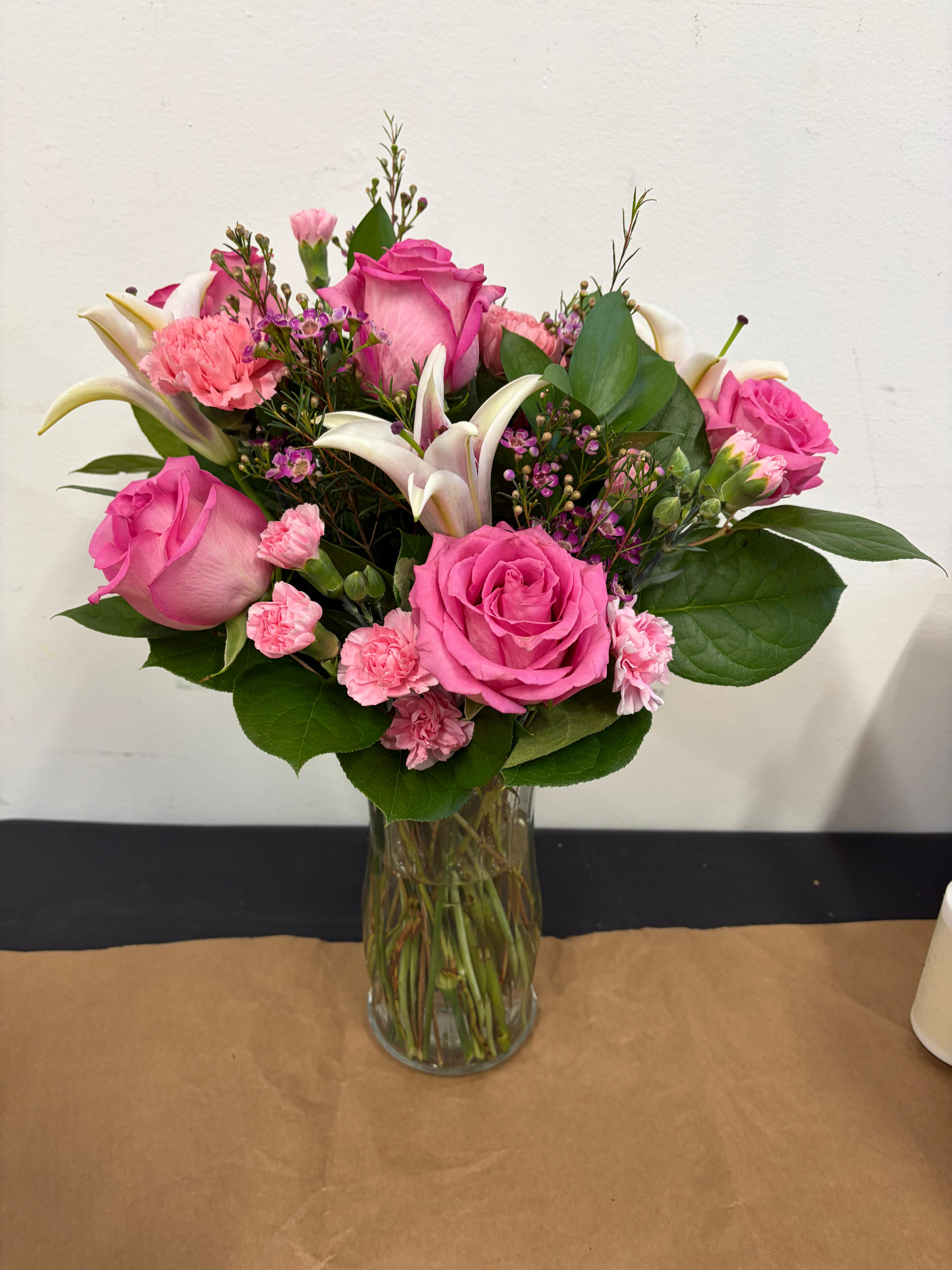 The Mariposa - Indulge in a whimsical dance of color with this vibrant, feminine arrangement. Featuring a stunning mix of premium hot pink roses and delicate lilies, The Mariposa is designed to capture the fluttering beauty of a garden in full bloom. Accented with ruffled carnations and lush greenery, this bouquet is the perfect way to send a message of joy, romance, or celebration.