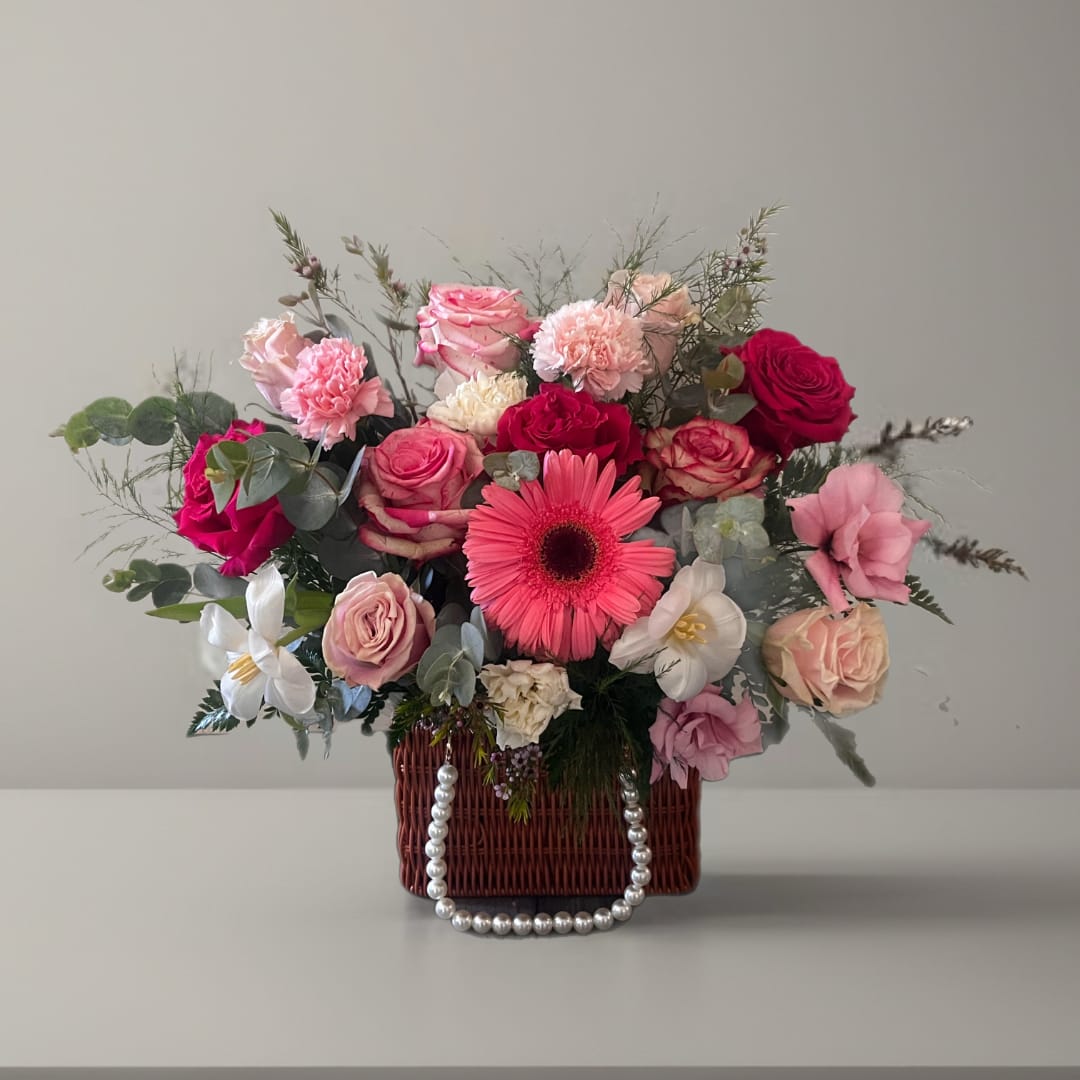 Mixed pink and white flower arrangement in a wicker basket with pearl handle
