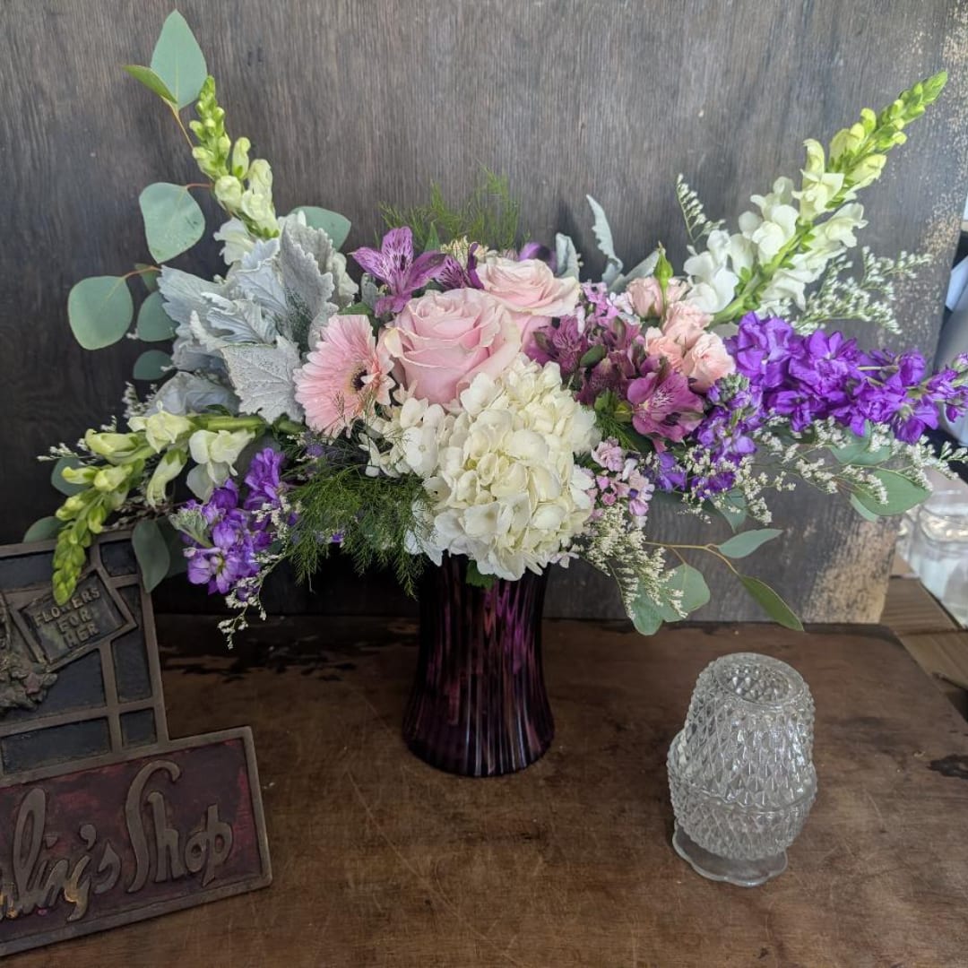 Pink and white floral arrangement in a purple vase with tall purple blooms