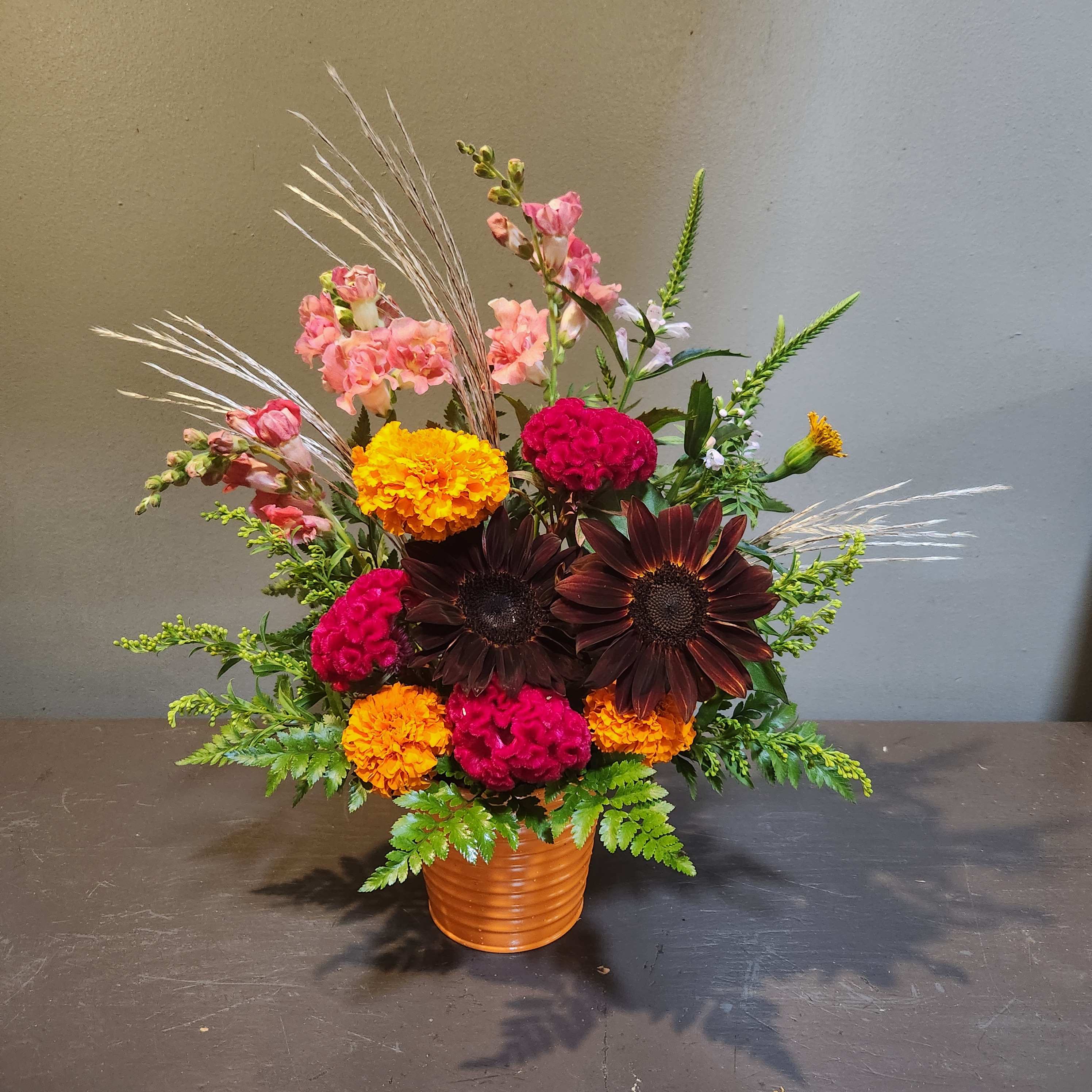 Mixed floral arrangement in a ribbed orange pot with pink, yellow, and dark blooms