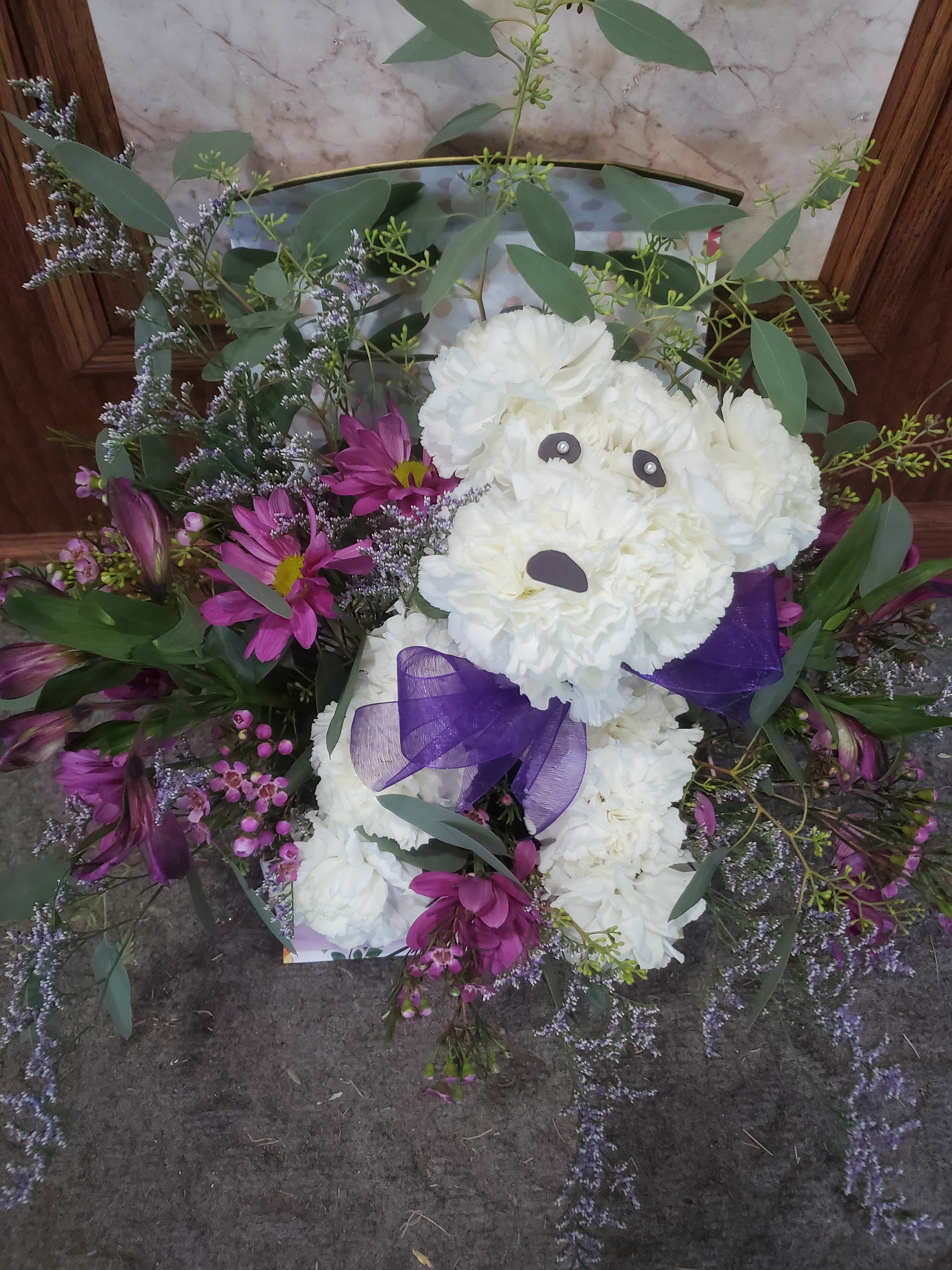 White teddy bear made of flowers with a purple bow and purple blooms