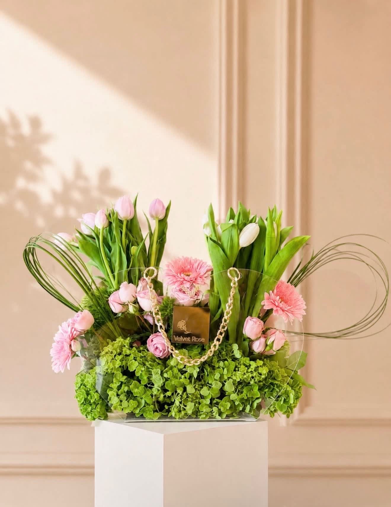 Pink tulips and roses arranged with pink daisies in a clear handbag-style container