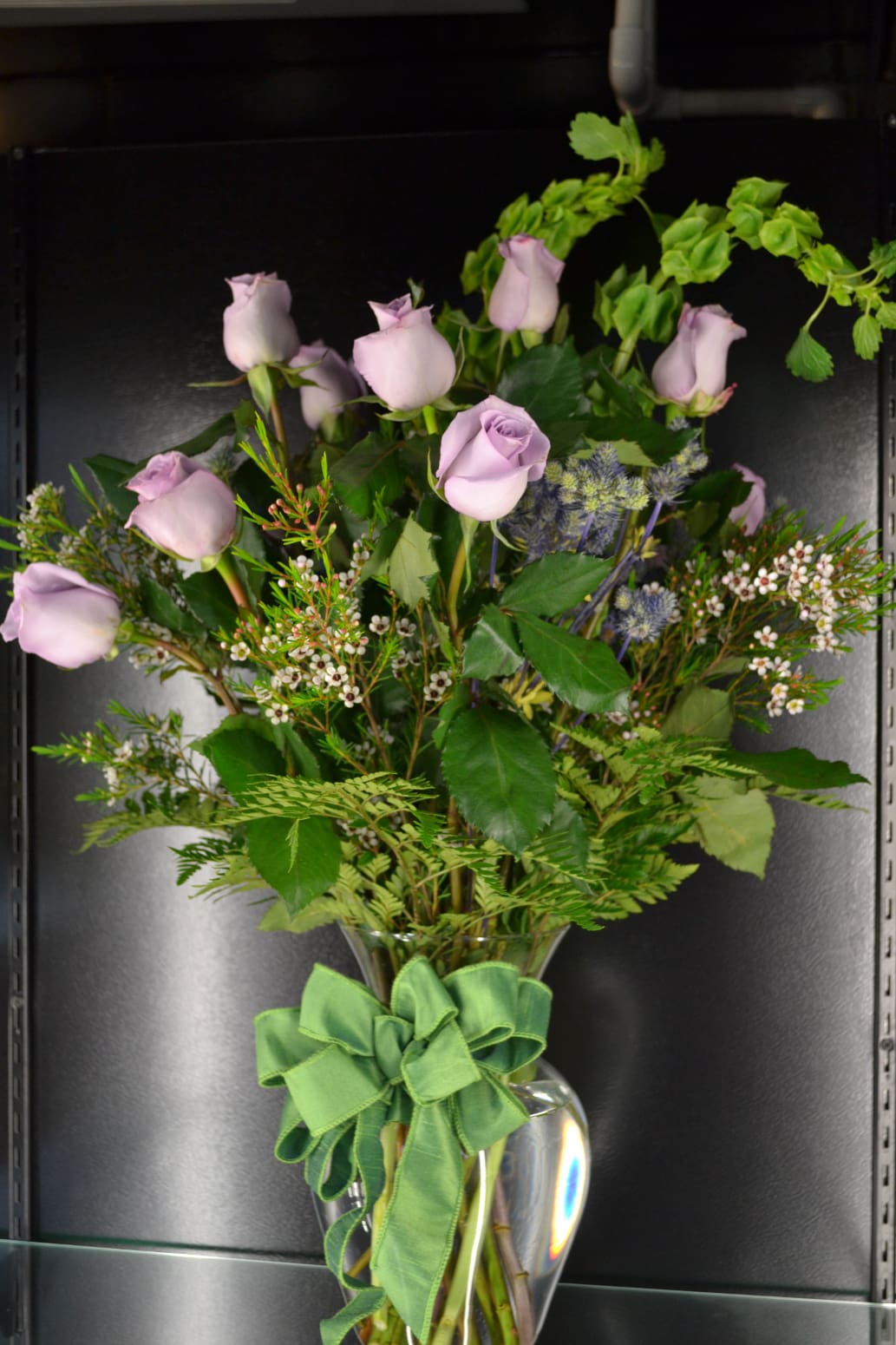 Lavender roses in a clear glass vase with a green ribbon
