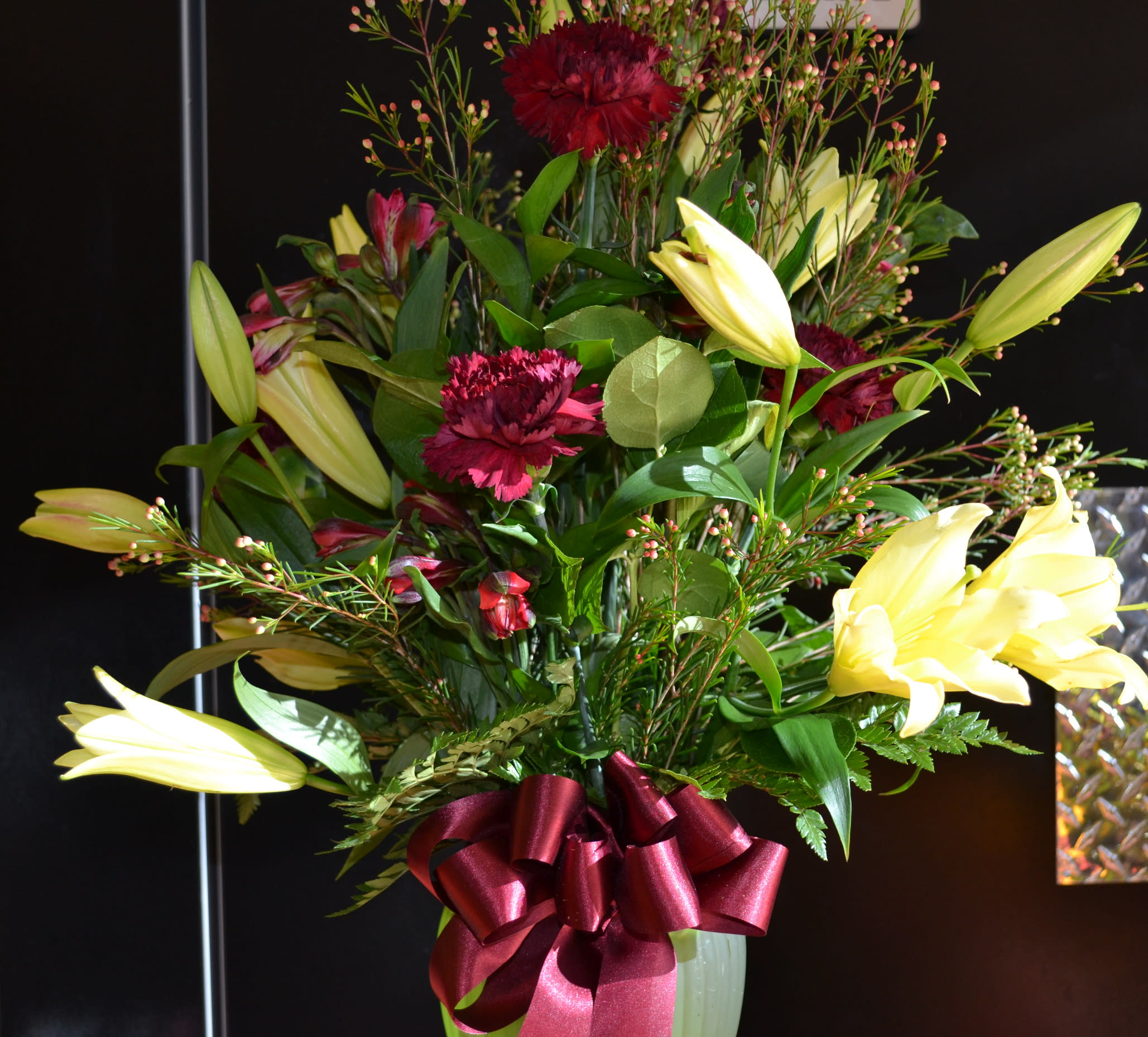 Bouquet of yellow lilies and burgundy carnations in a vase with a red ribbon