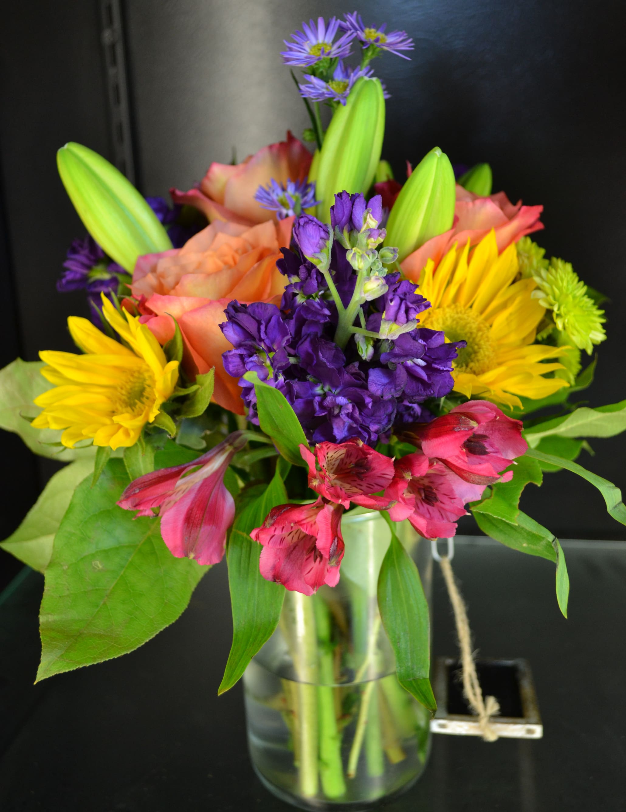 Colorful bouquet of lilies, sunflowers, and purple flowers in a glass vase