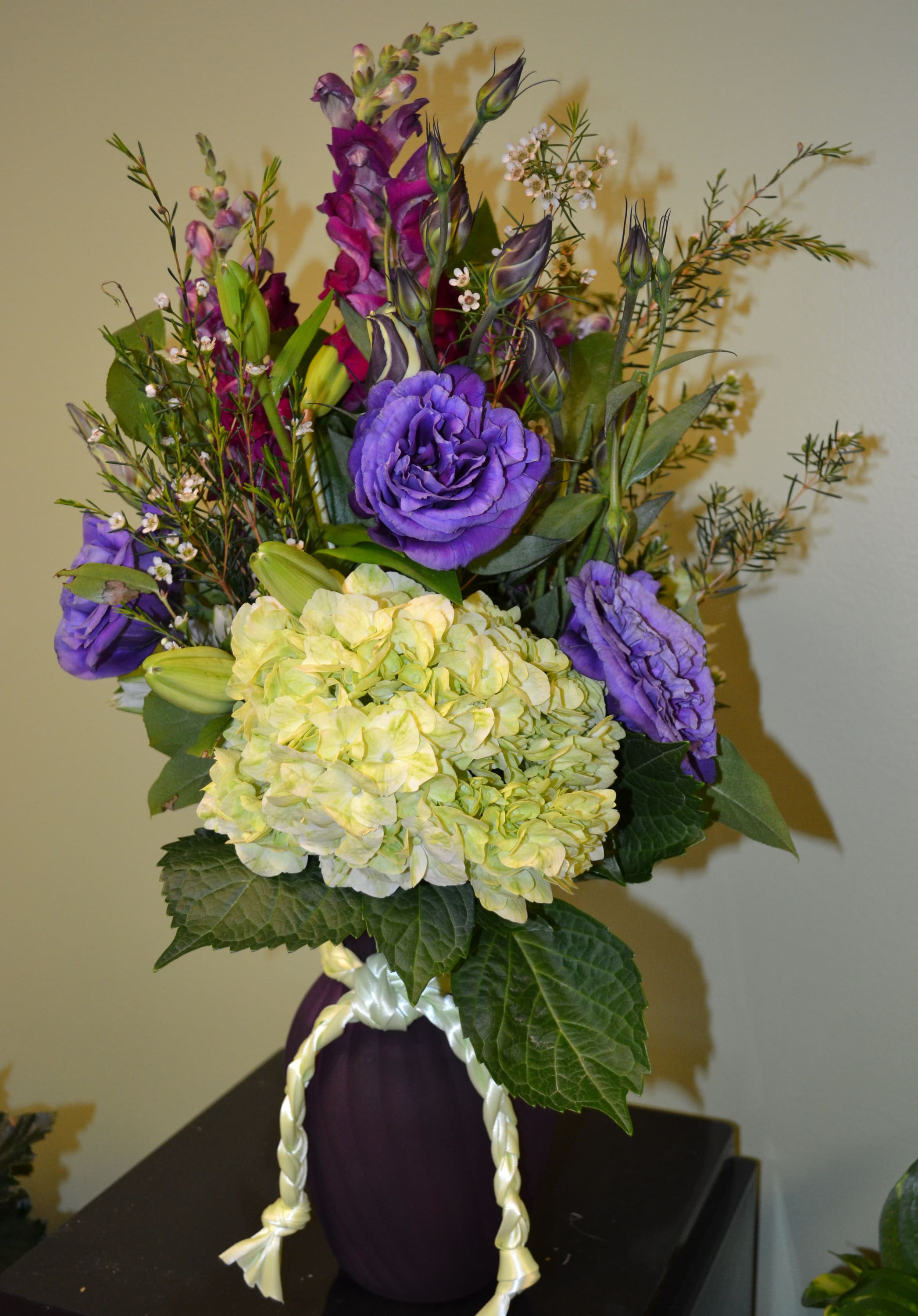Purple and yellow floral arrangement in a dark vase with a braided ribbon handle