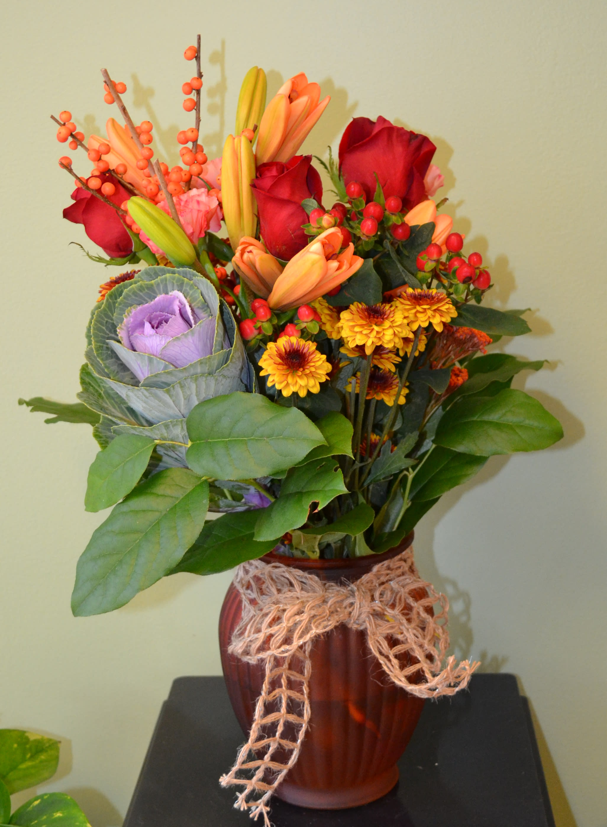 Capture Fall - This stunning arrangement is sure to add a smile to any recipient's face! Flowering Kale, Orange Winterberries, fall color Poms, Red Roses, Orange Lilies, Orange Yarrow, Red Hypericum Berries and more! *Kale may be replaced by something like Hydrangea.
