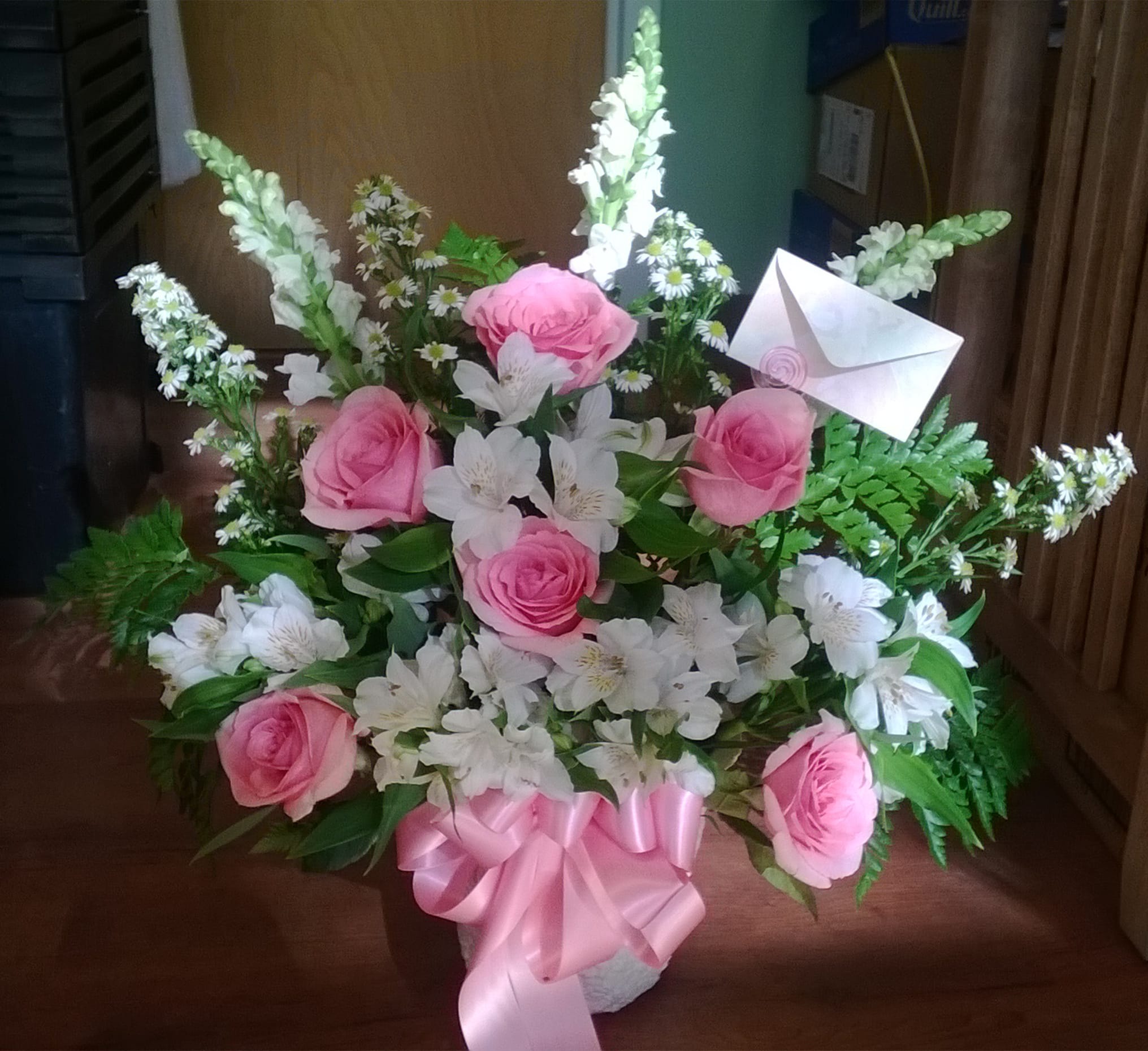 Pink roses and white flowers in a basket with a pink ribbon and envelope card