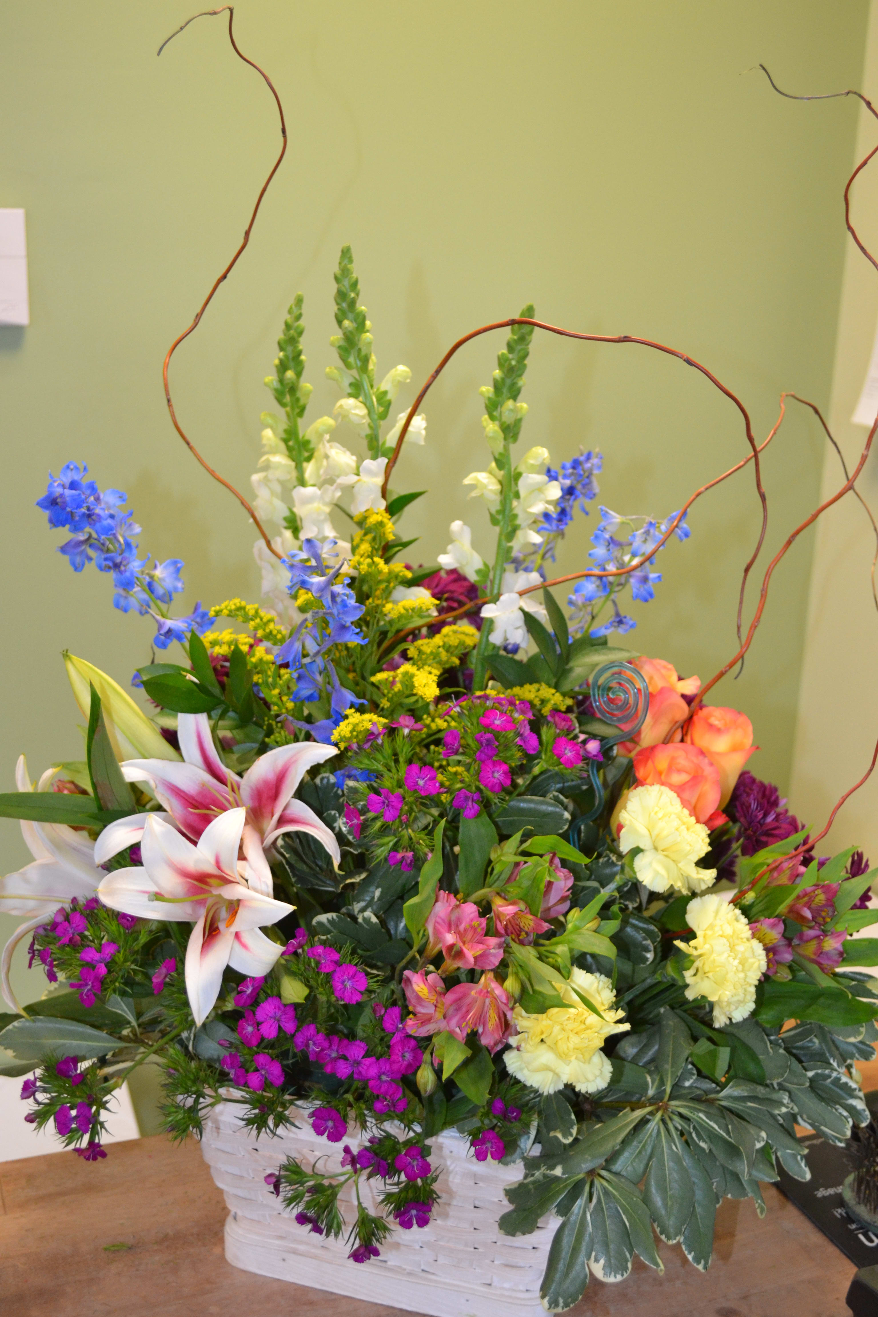 Colorful mixed flower arrangement in a white basket with tall curly branches