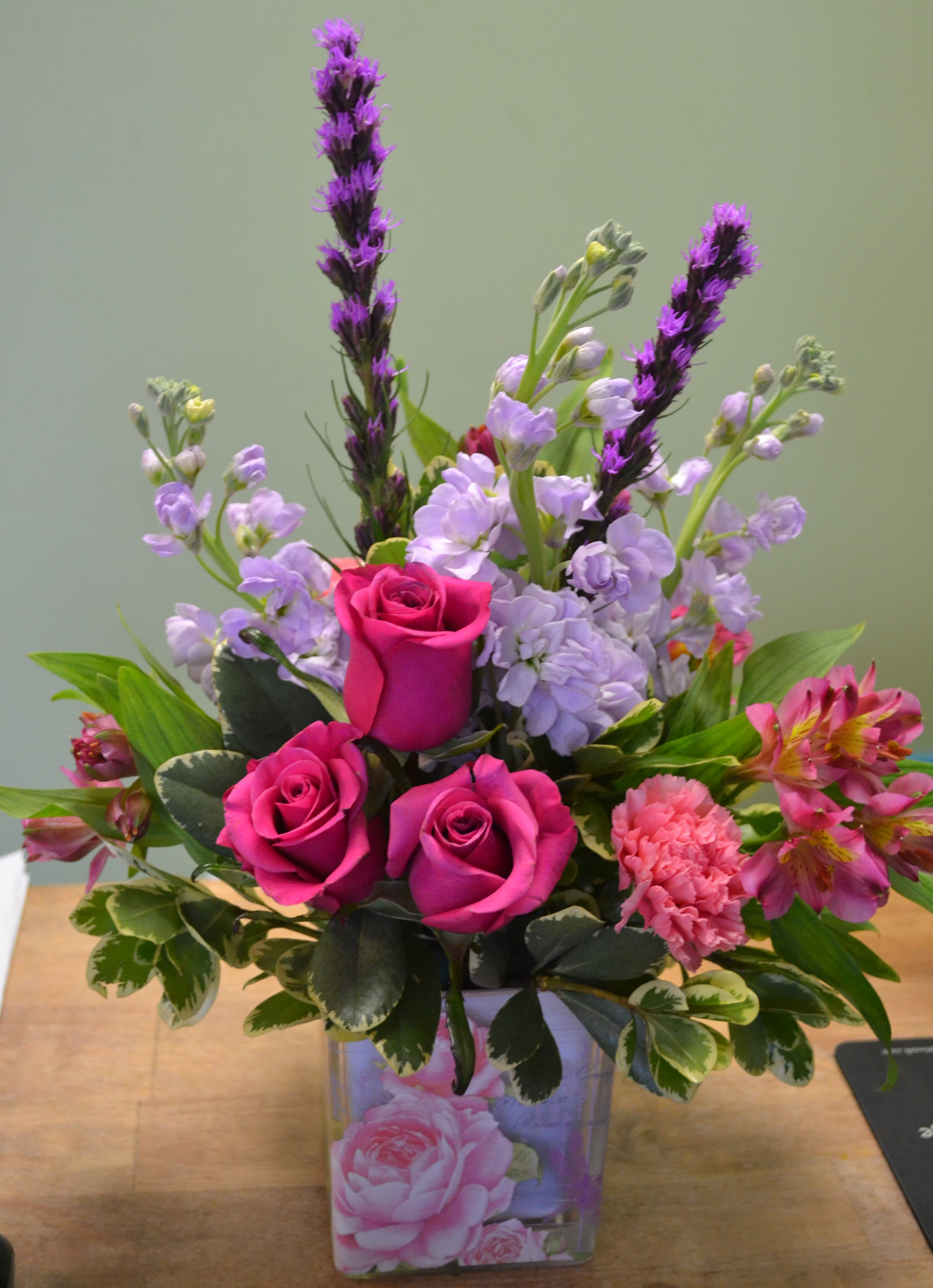 Pink roses and lavender flowers arranged in a clear square vase