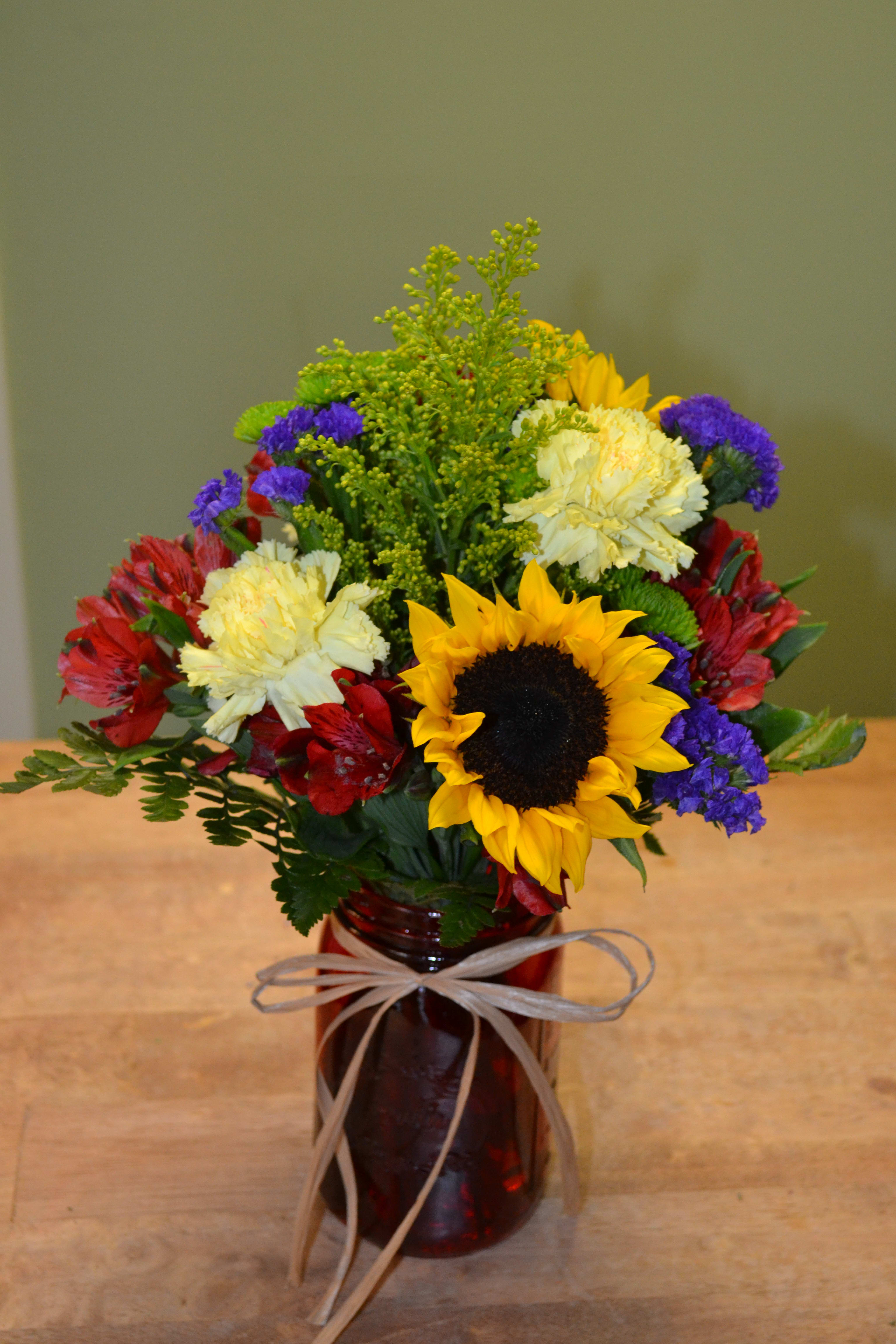 Mixed bouquet in a red glass vase with a sunflower and carnations
