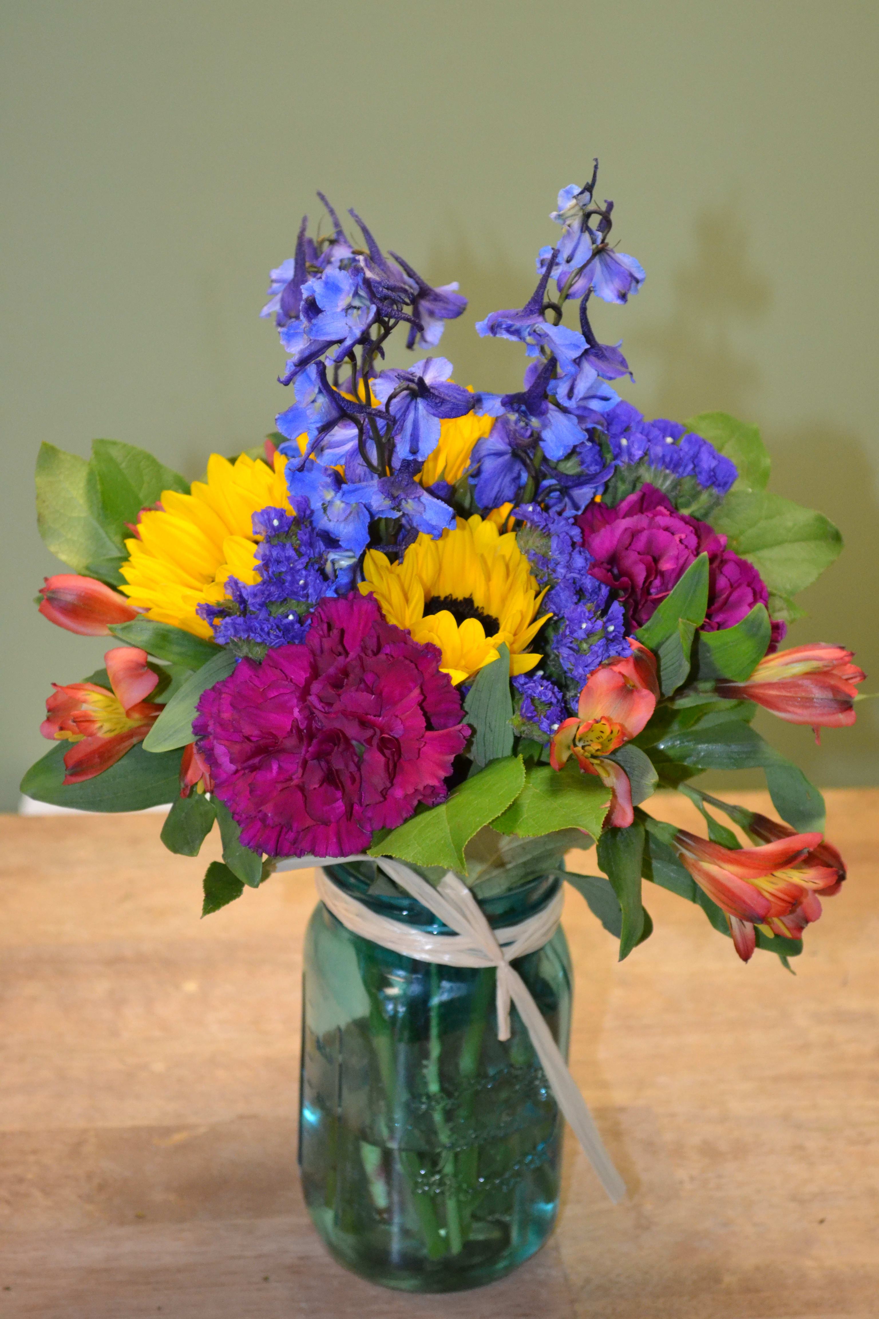 Colorful bouquet in a blue glass jar with a ribbon tie