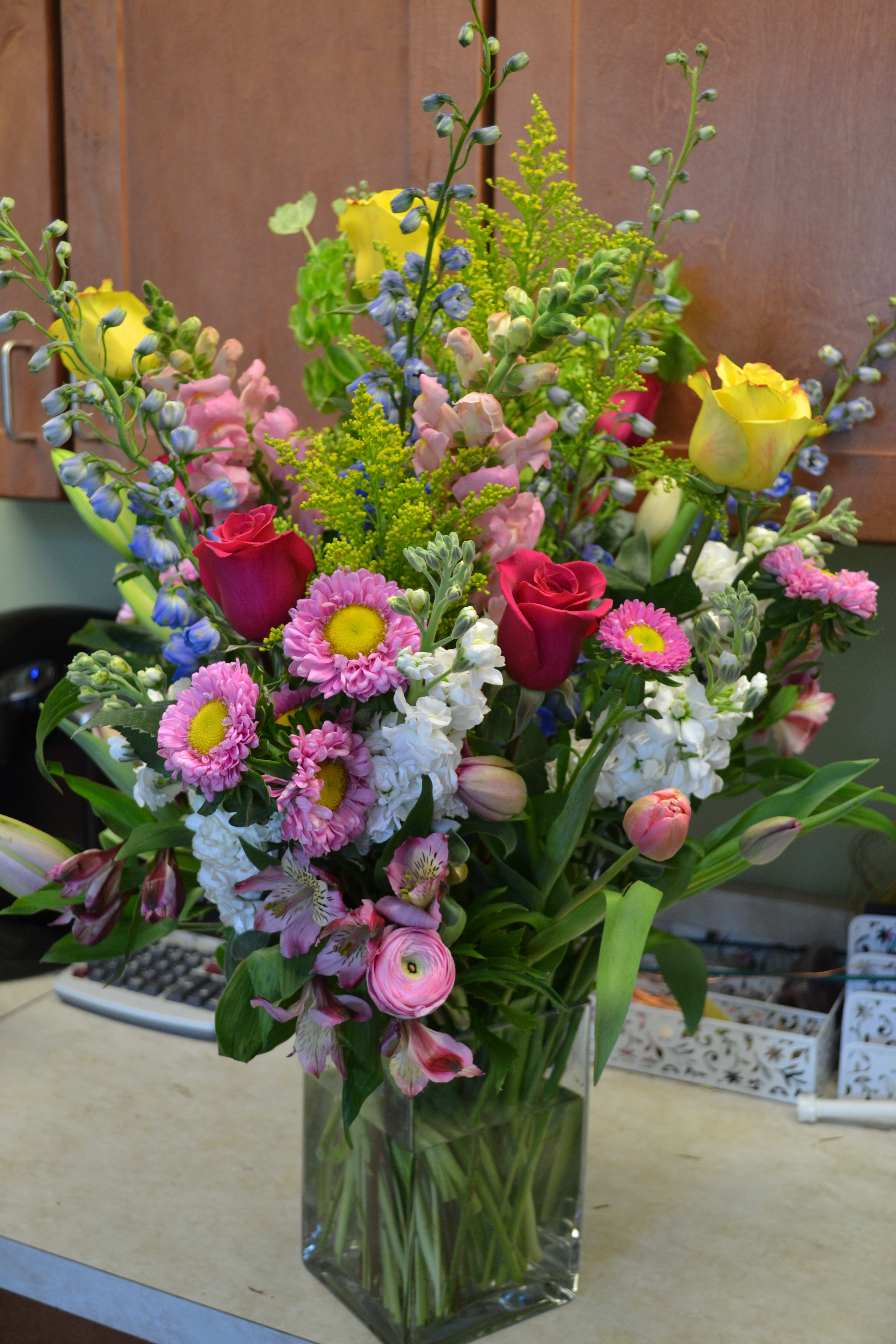 Mixed bouquet of roses, daisies, and snapdragons in a glass vase