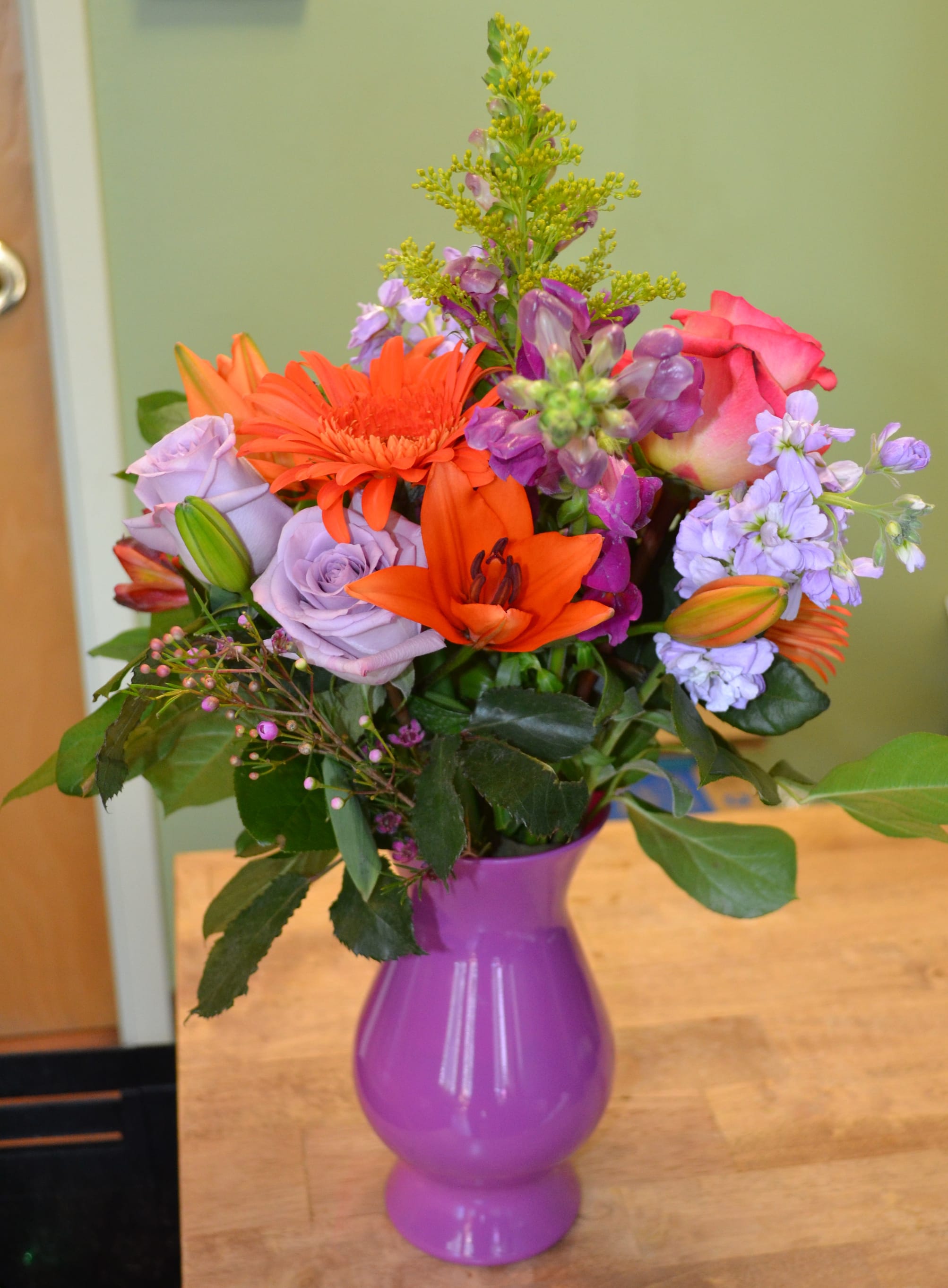 Mixed bouquet of orange, pink, and lavender flowers in a purple vase