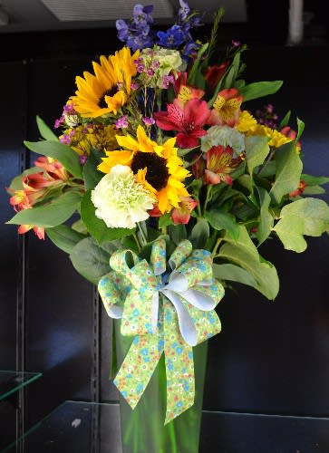 Tall mixed bouquet with sunflowers, lilies, and a decorative bow in a green vase