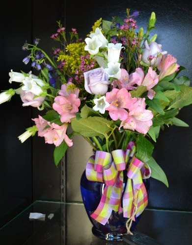 Mixed bouquet of pink, white, and lavender flowers in a blue vase with a plaid ribbon