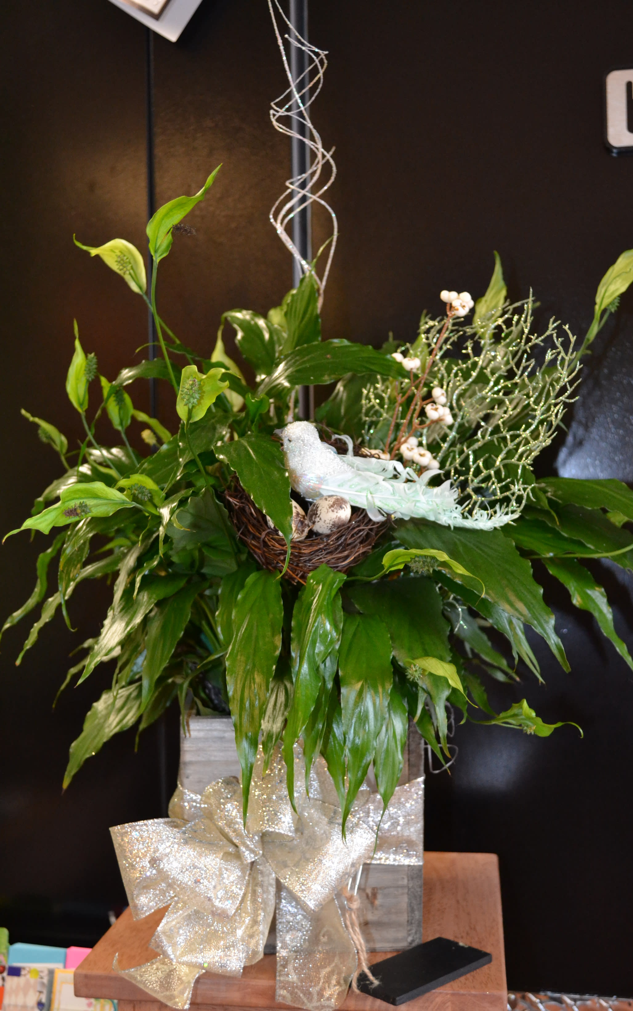 Green floral arrangement with calla lilies and a glittery bow in a box