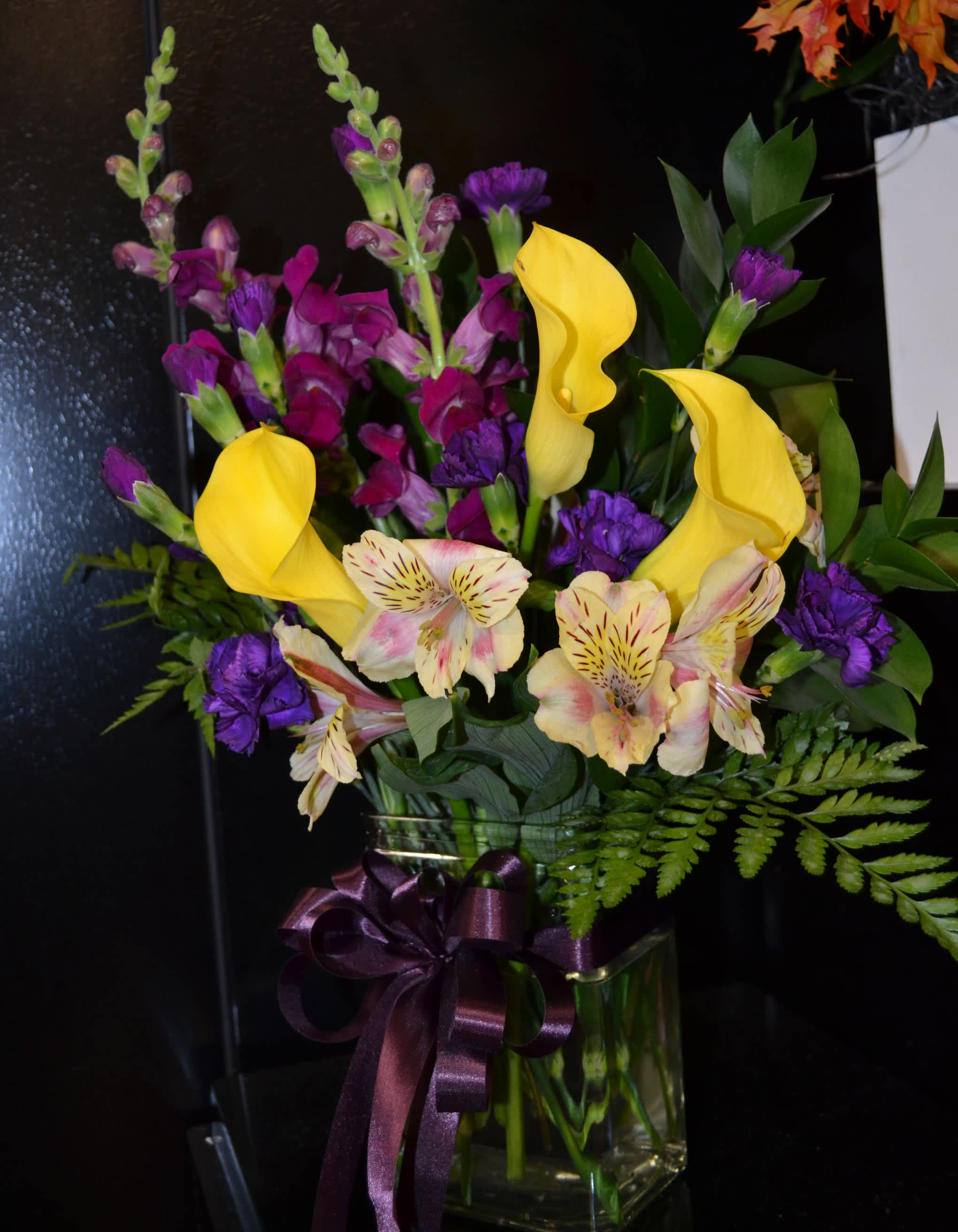 Bouquet of yellow calla lilies, purple flowers, and striped alstroemeria in a glass vase