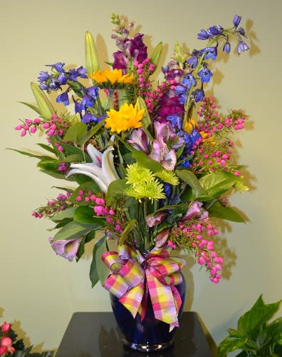 Colorful mixed flower arrangement in a blue vase with a plaid ribbon