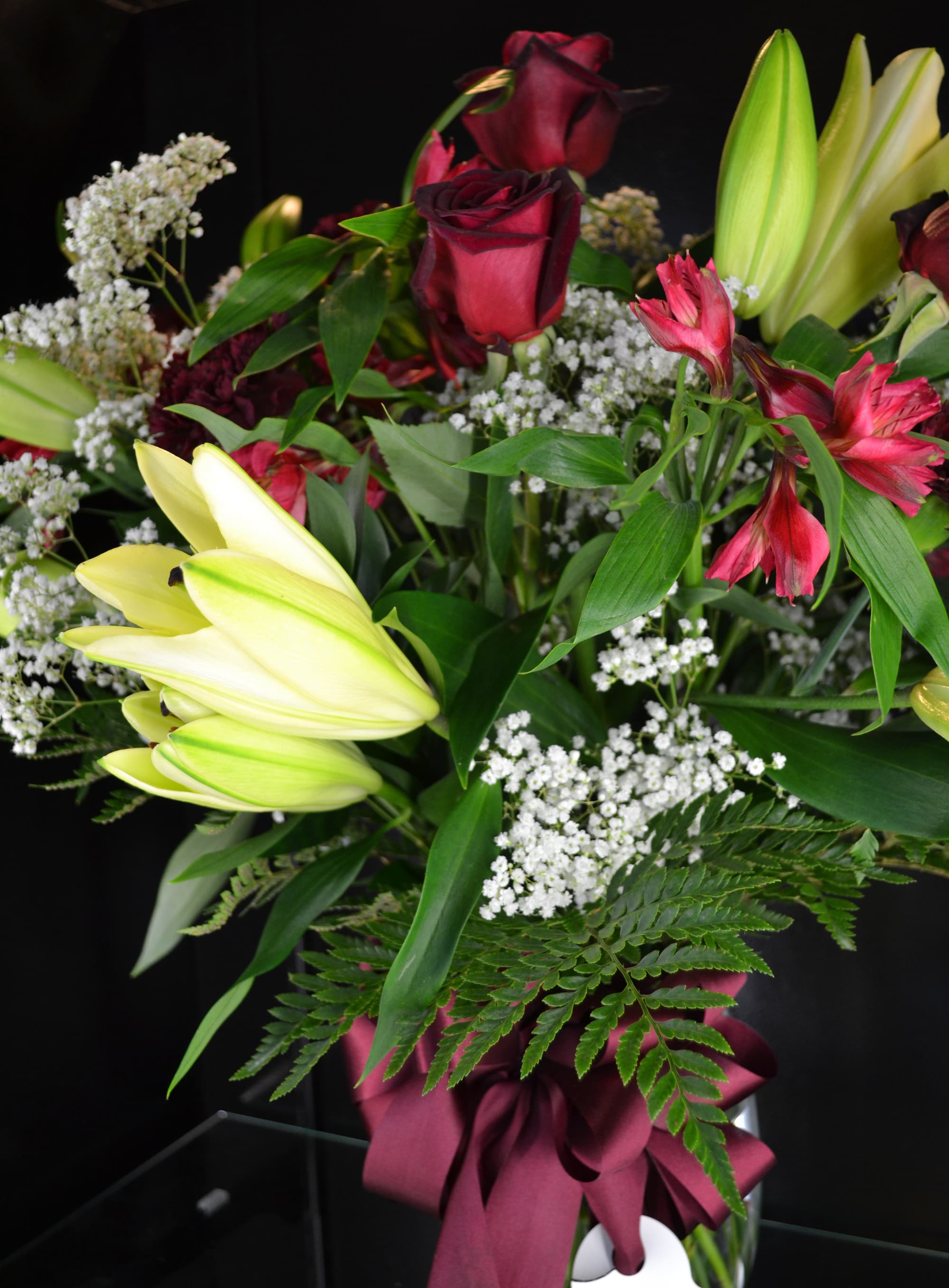 Bouquet of burgundy roses and pale lilies with white filler flowers