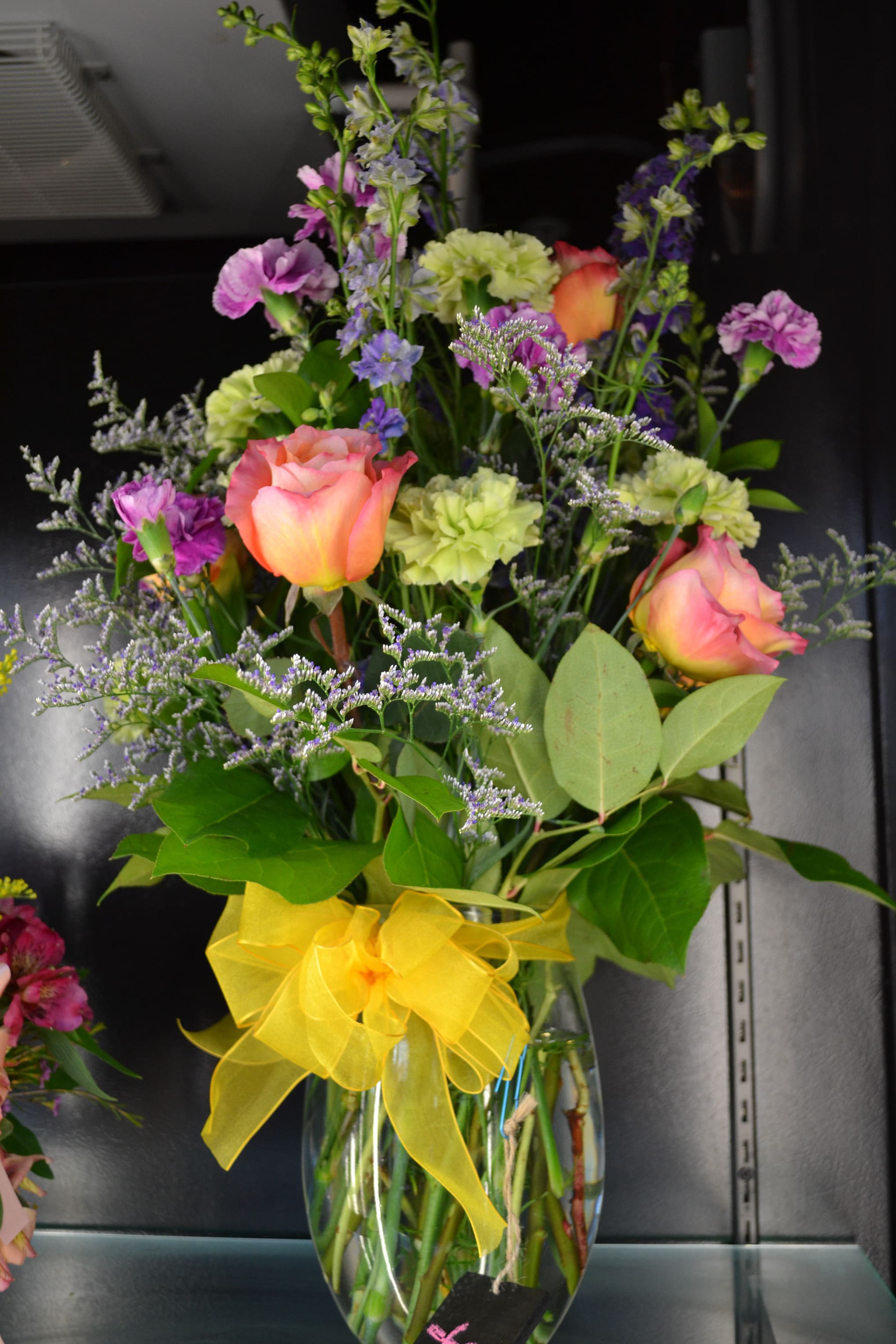 Mixed bouquet of roses and purple flowers in a glass vase with a yellow bow
