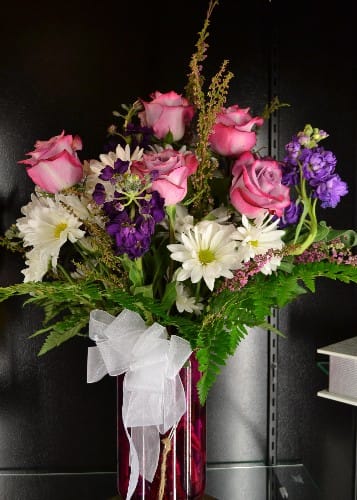 Pink roses and white daisies in a red vase with a white bow