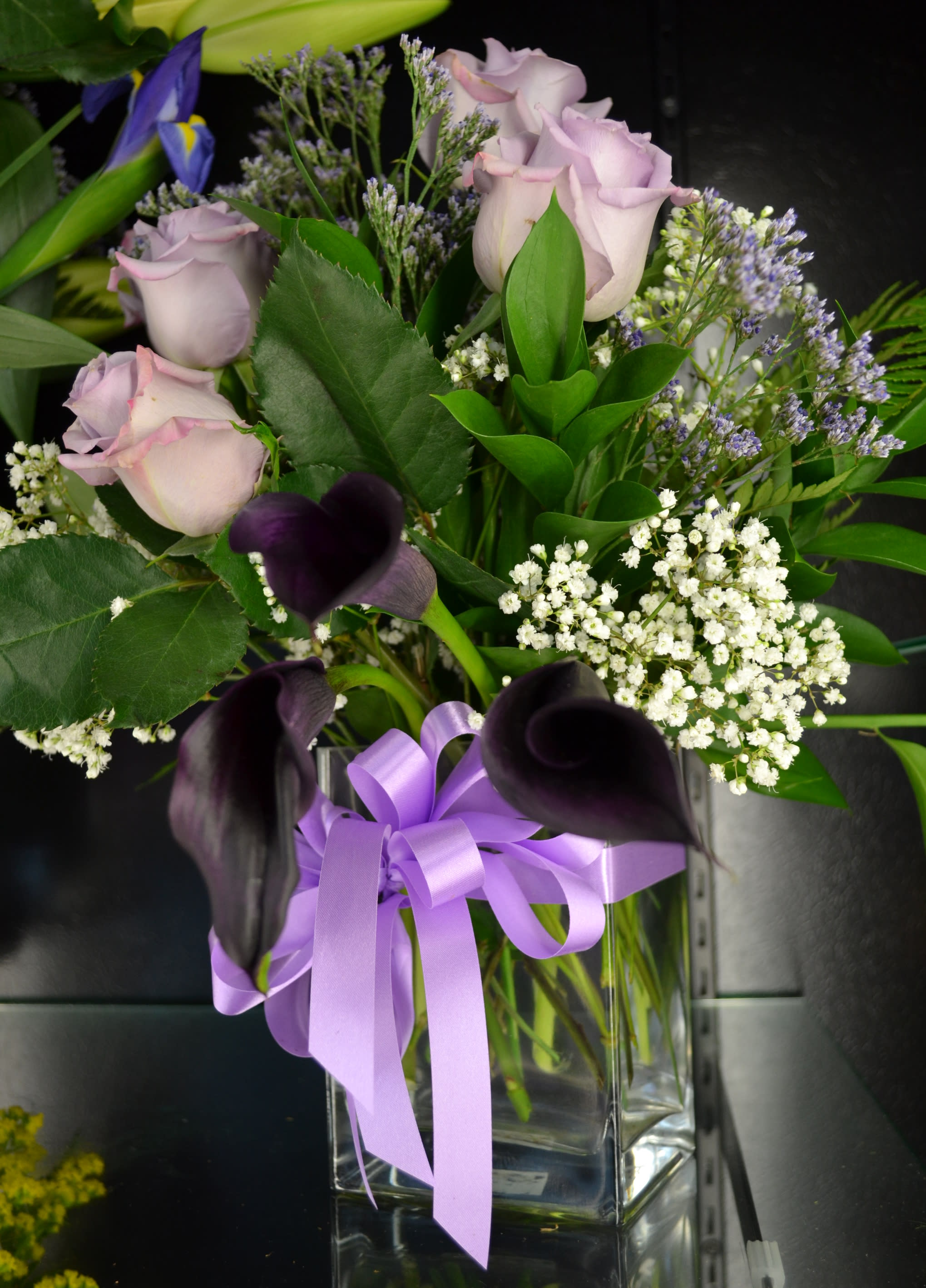 Lavender roses and dark calla lilies in a glass vase with a purple ribbon
