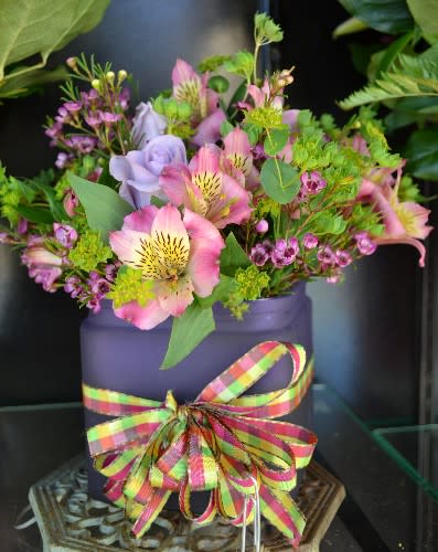 Pink and lavender flowers in a purple container with a plaid ribbon