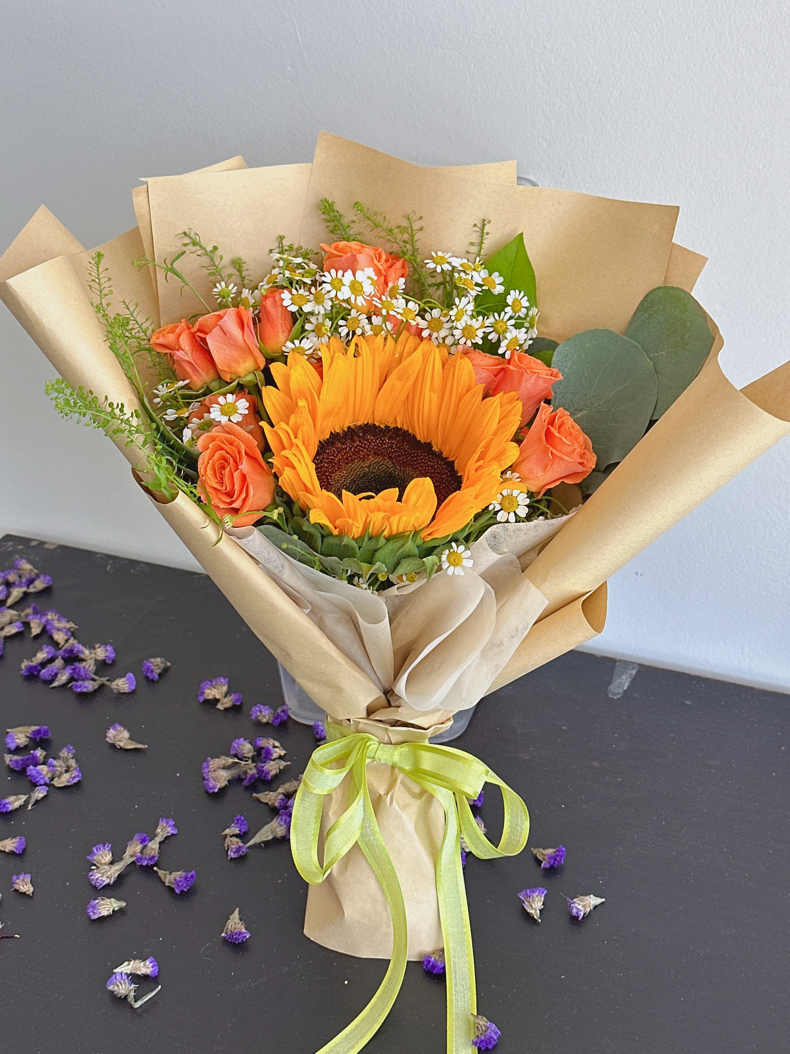 Bouquet with a sunflower, orange roses, and small white daisies in kraft paper