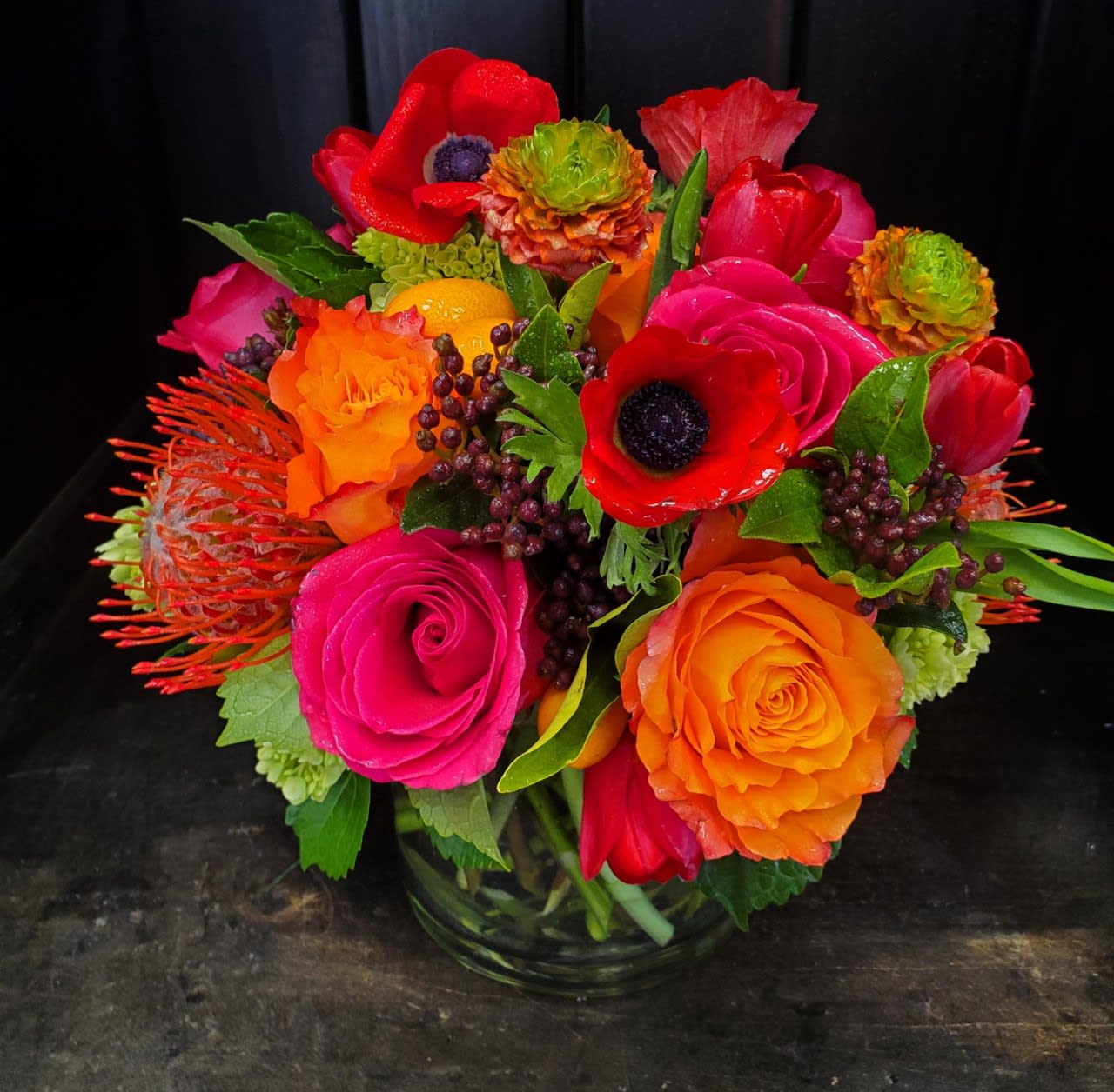 Bright mixed bouquet of red, pink, and orange flowers in a glass vase