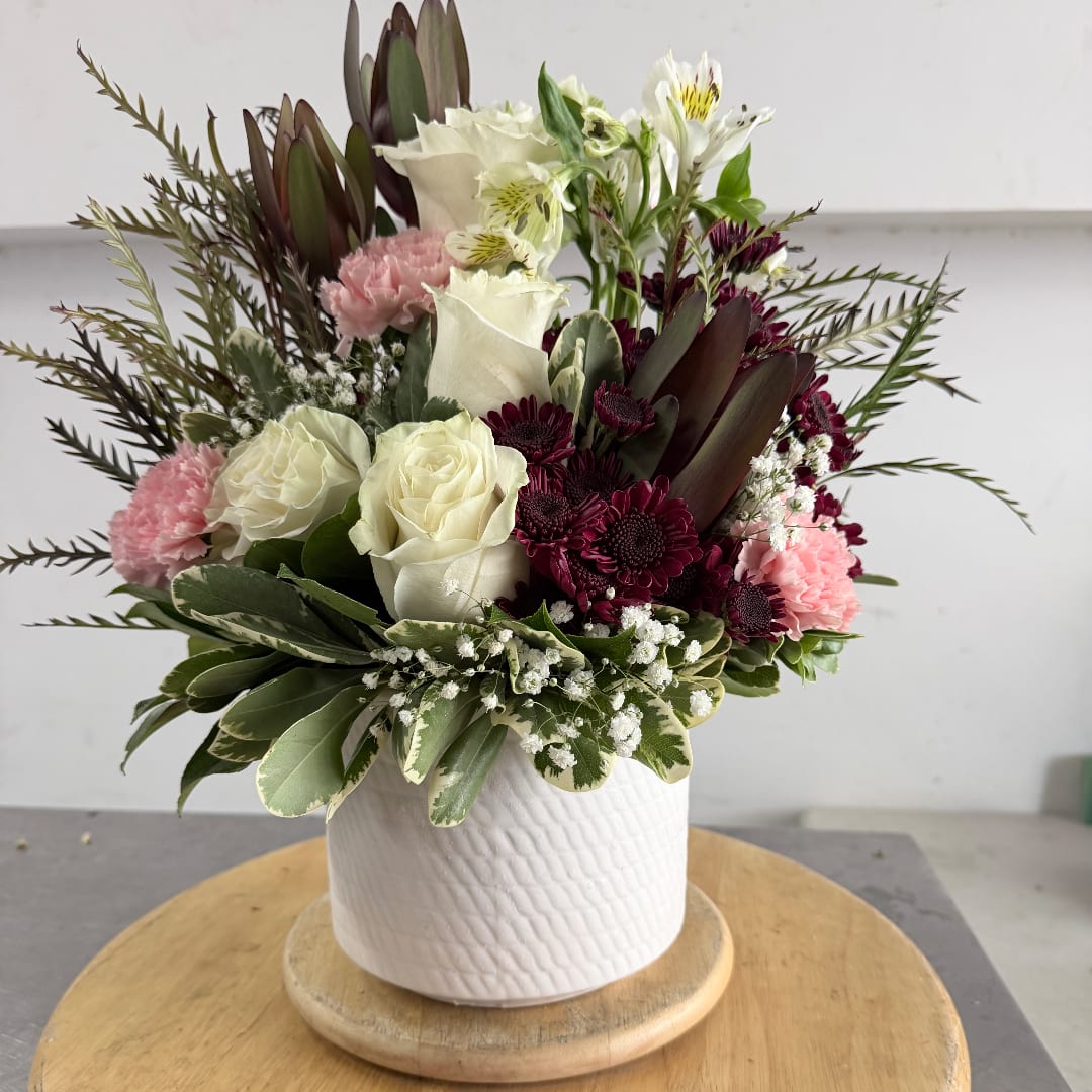 Mixed bouquet of white roses, pink carnations, and burgundy blooms in a white vase