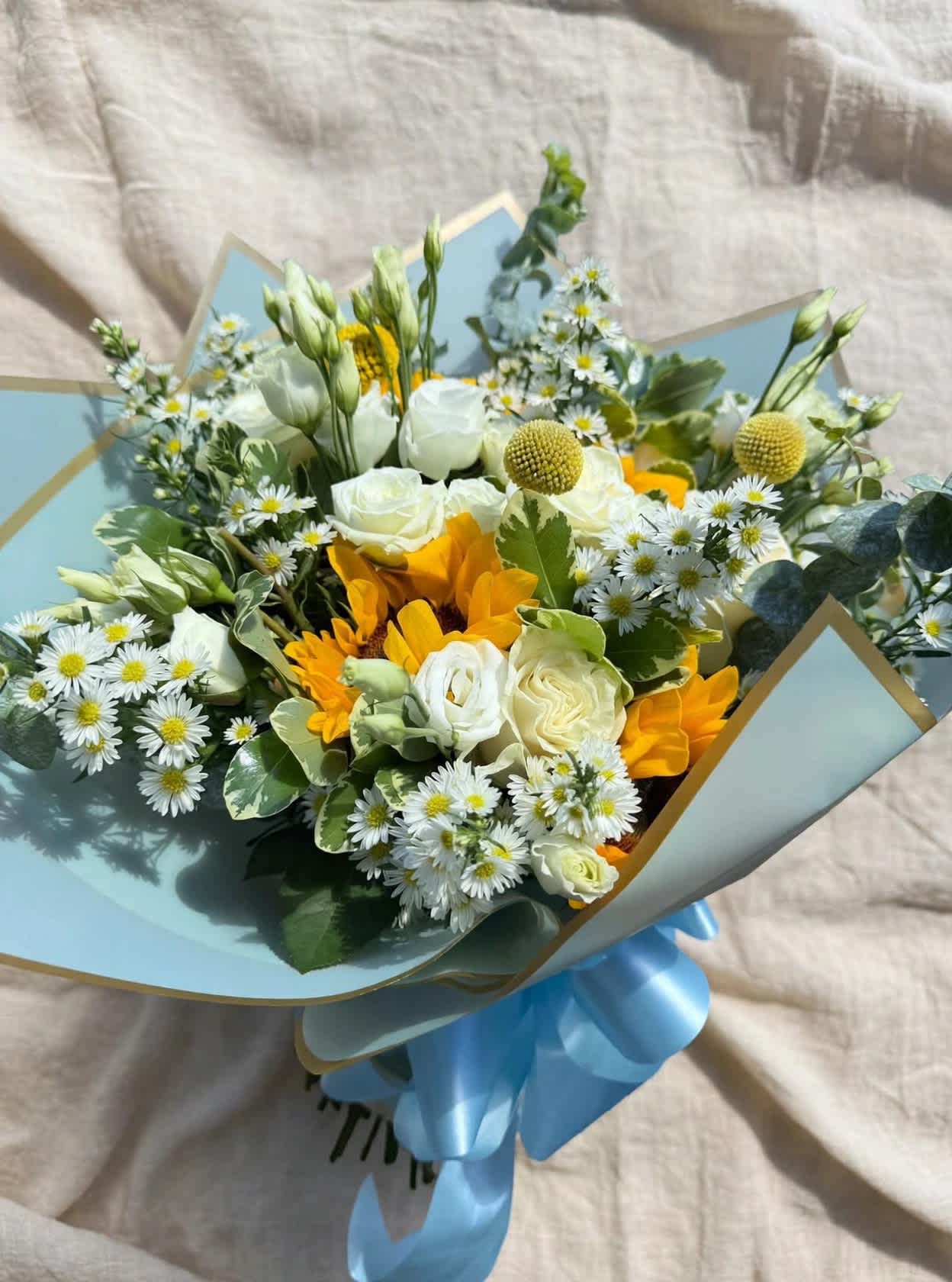 Bouquet of white and yellow flowers wrapped in pale blue paper with a blue ribbon
