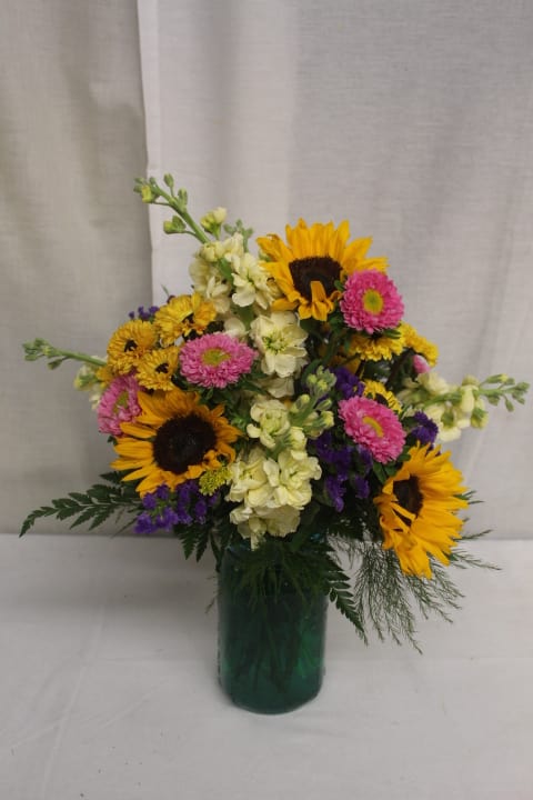 Mixed bouquet with sunflowers, pink daisies, and cream flowers in a green vase