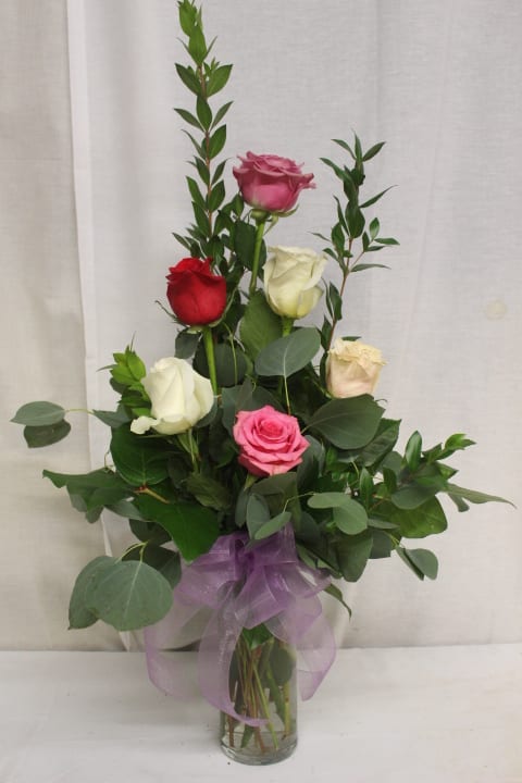 Bouquet of multicolored roses in a clear glass vase with a purple ribbon